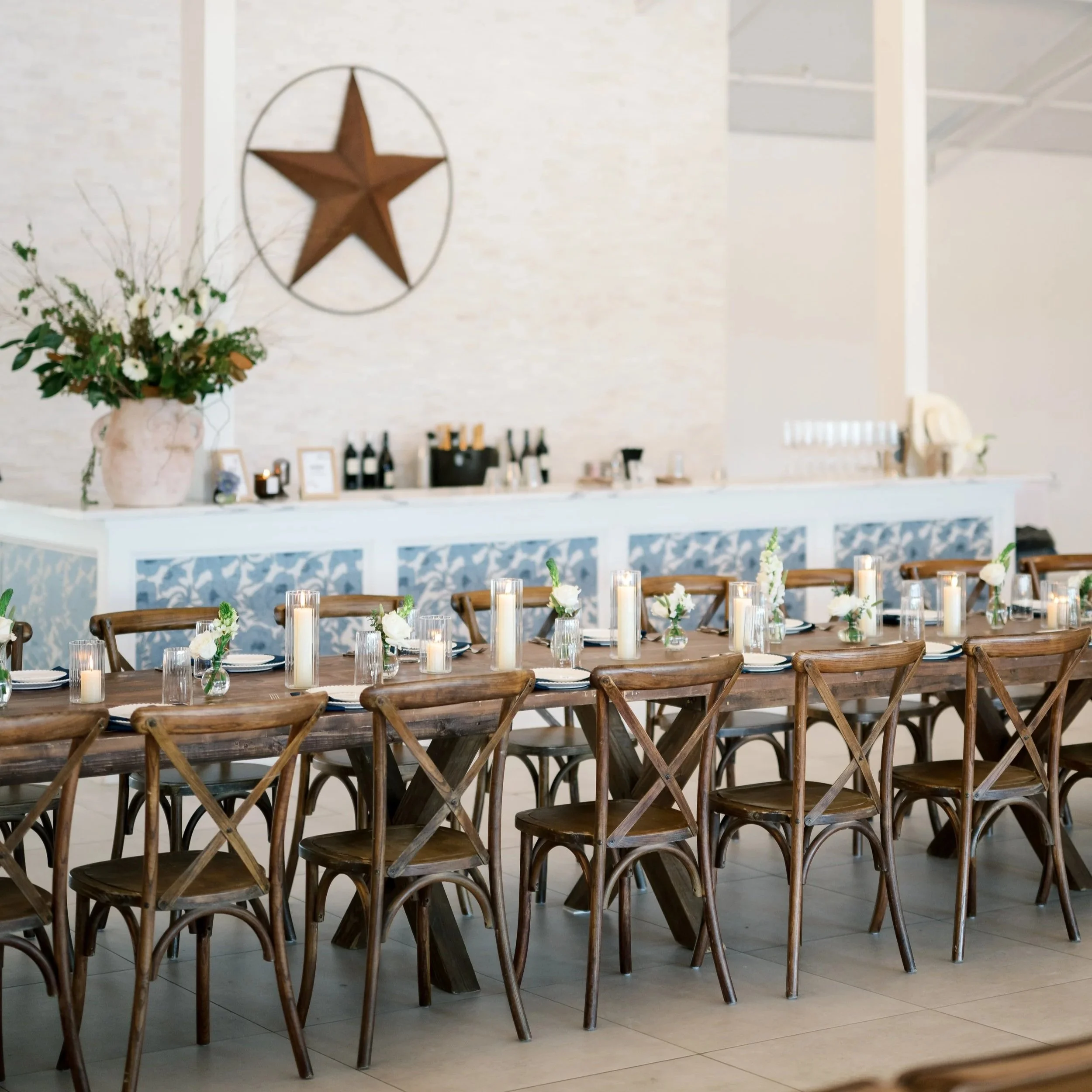 A rehearsal dinner and welcome party at The Stables set up for a Texas Chic themed dinner. The Stables is complete with a built-in bar, included farmhouse tables and cross back chairs, and in-house beverage service. The Stables is a modern barn venue