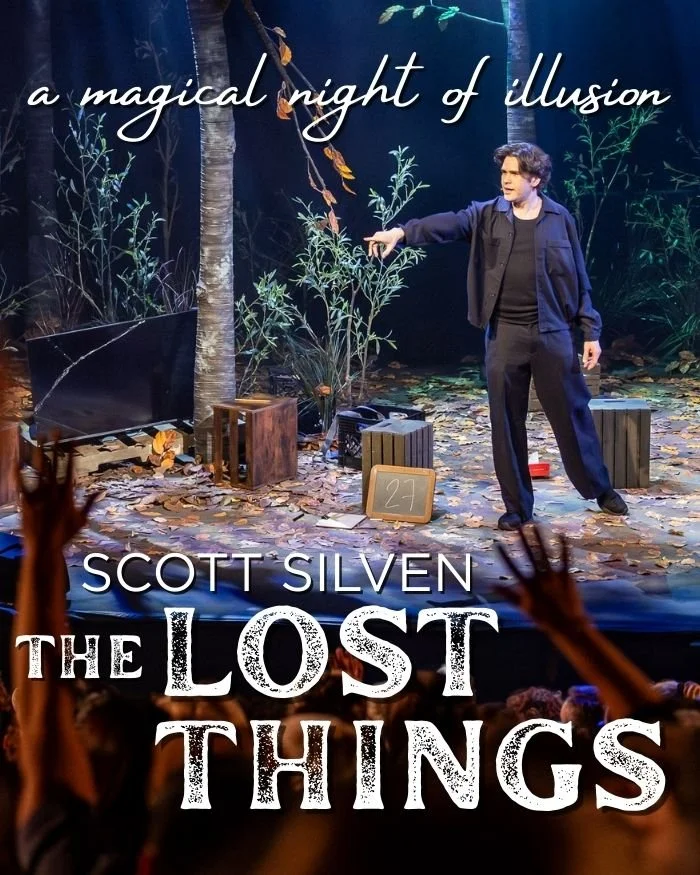 A stage set with a man in dark clothing pointing at a small plant, surrounded by forest-themed props, with the title "The Lost Things" and a tagline "a magical night of illusion" displayed above.