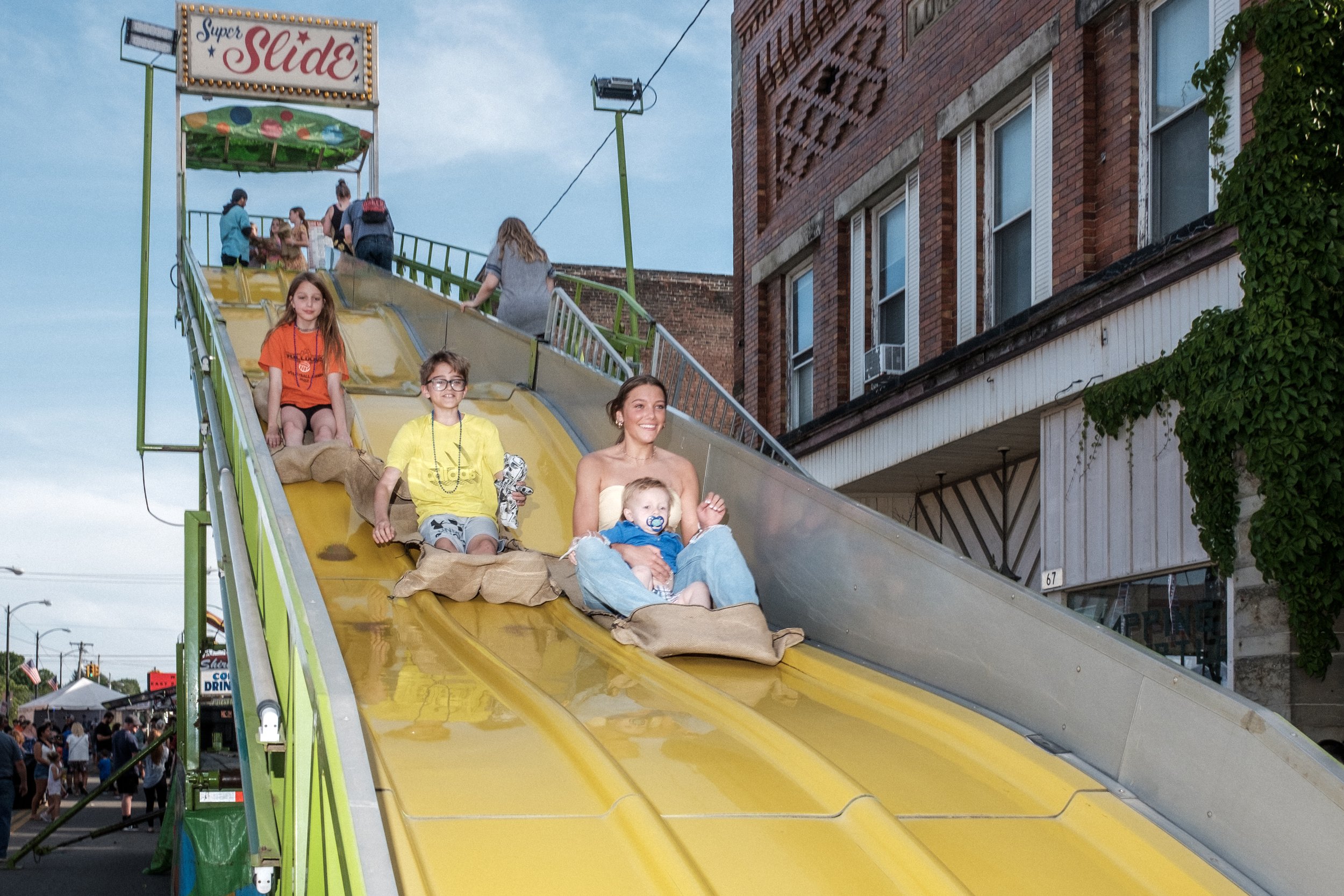 Hanna Gaither of Newcastle, Ohio, and Miles McCoy (in her lap) ride down a slide at the East Palestine Street Fair on May 27, 2023. The annual Memorial Day Celebration was paid for by Norfolk Southern.