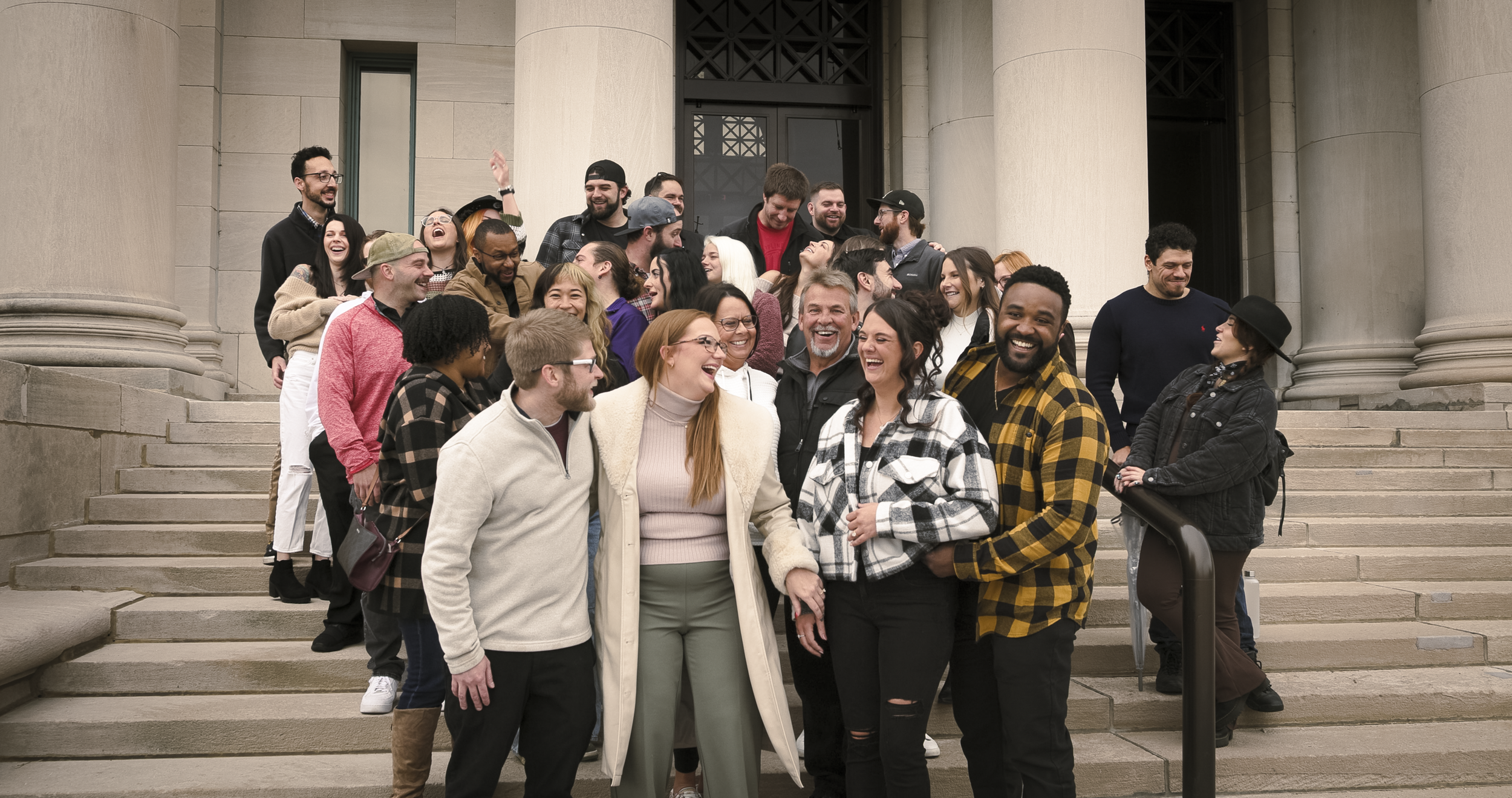A group of diverse people gathered on the steps of a building, smiling, laughing, and enjoying each other's company.