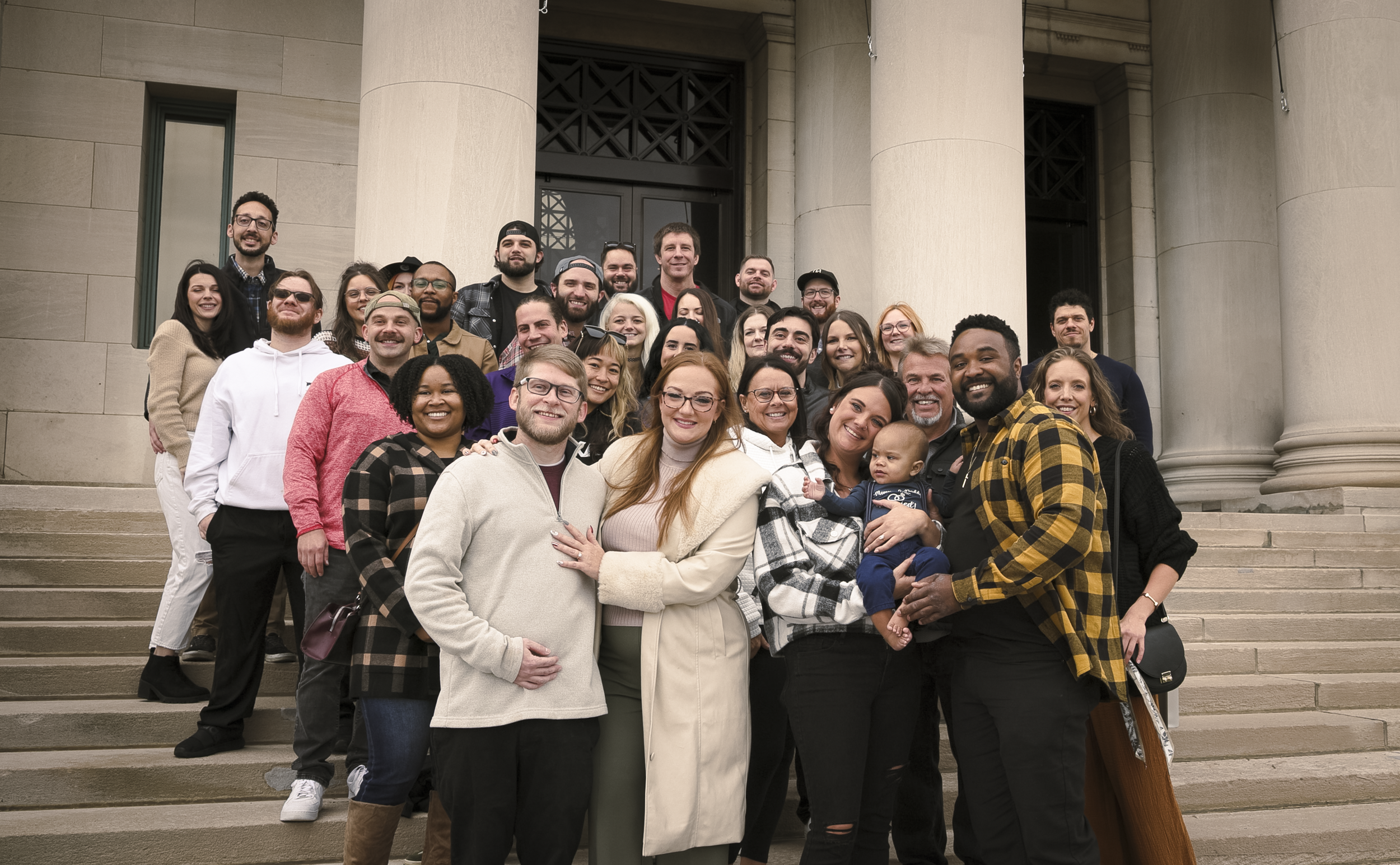 Group of diverse people standing on steps in front of a building with large columns, smiling for a photo.