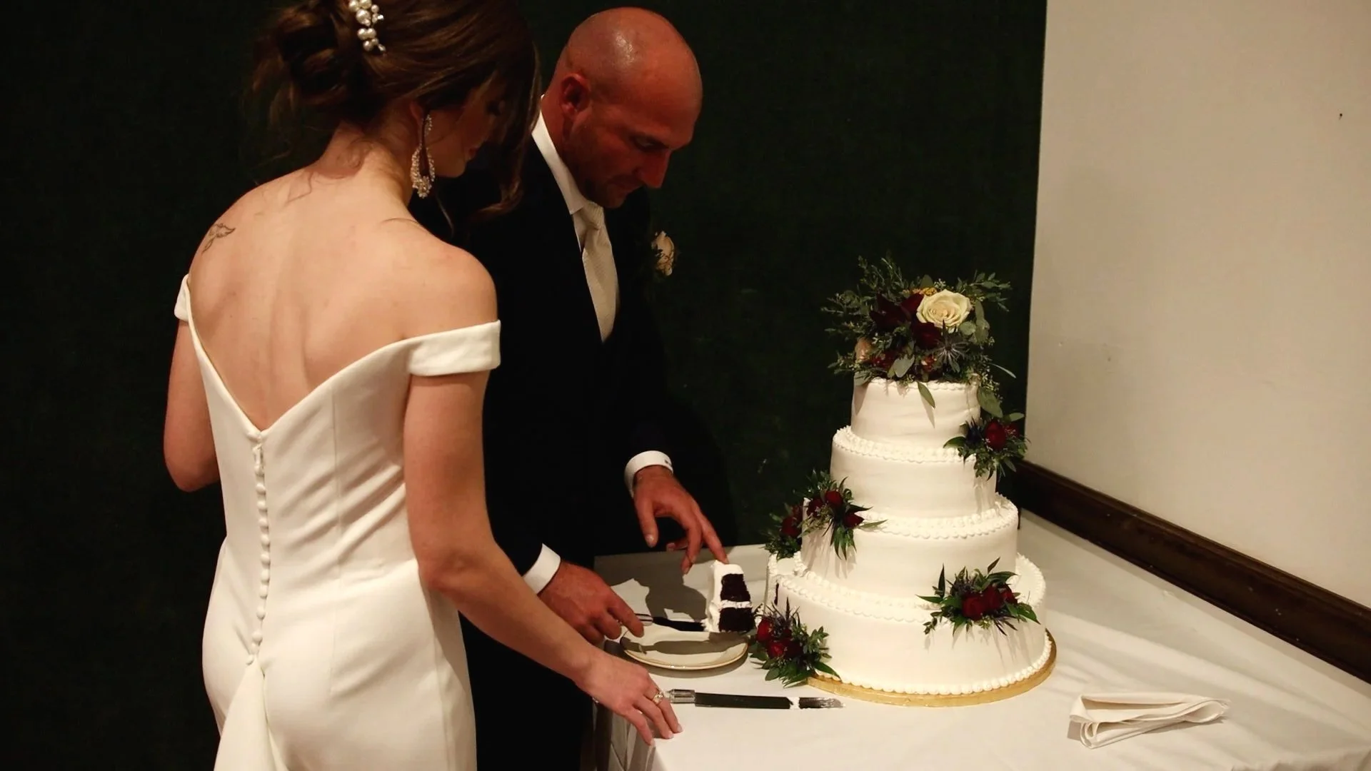 A bride and groom cutting a multi-tiered wedding cake decorated with roses and greenery.