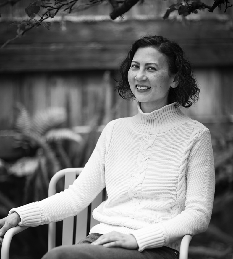 Mandy Ma, Executive Assistant at Julie Rootes Interiors, smiles in a black dress, surrounded by vibrant trees.