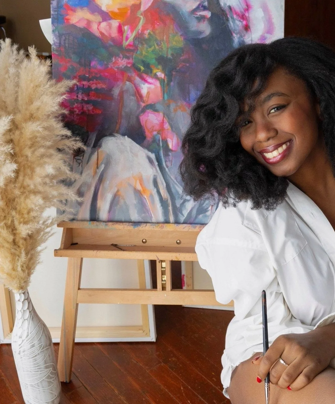 Alexis Marie smiling and sitting in front of an unfinished painting