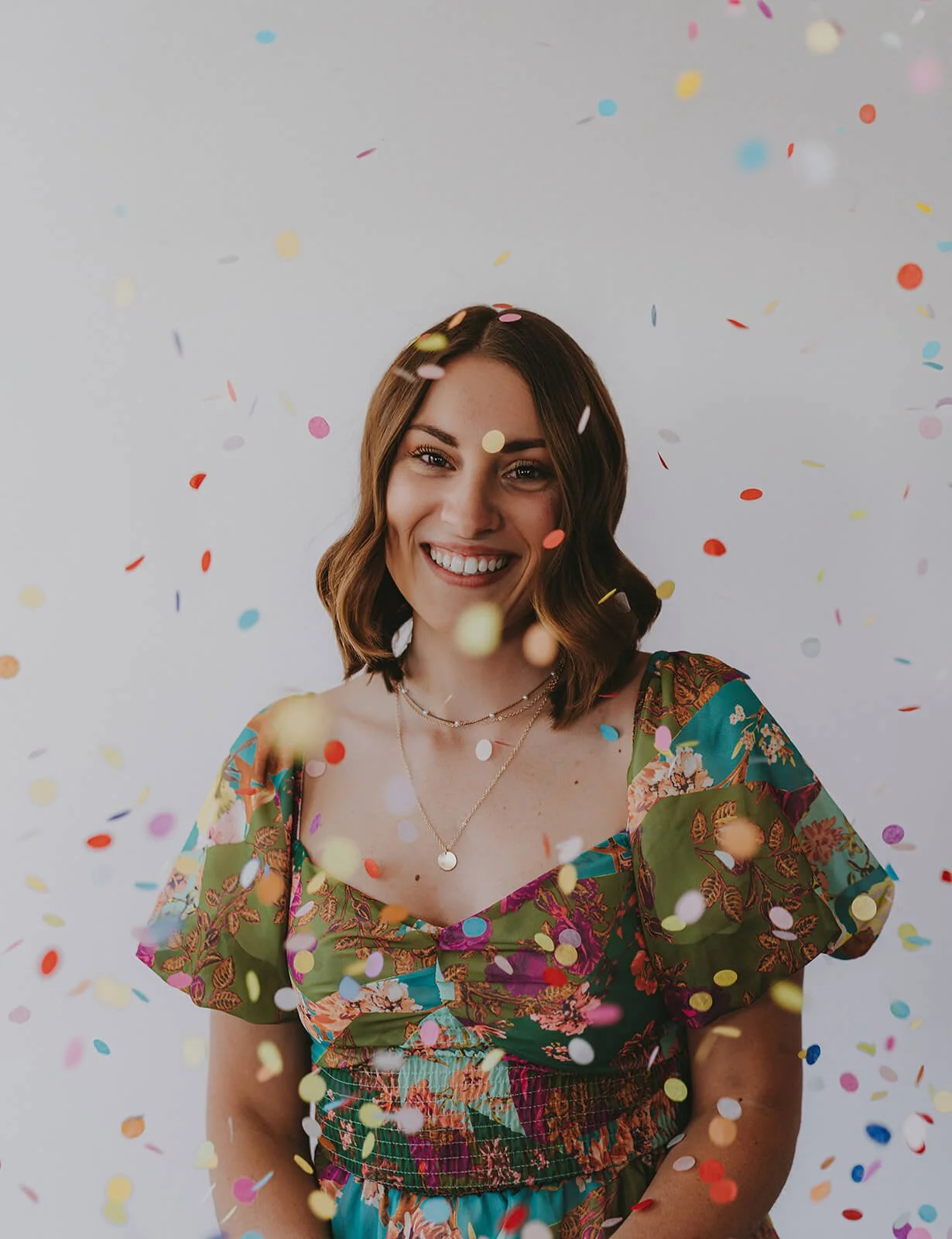 Woman in a multi colored dress smiling in a swirl of confetti.