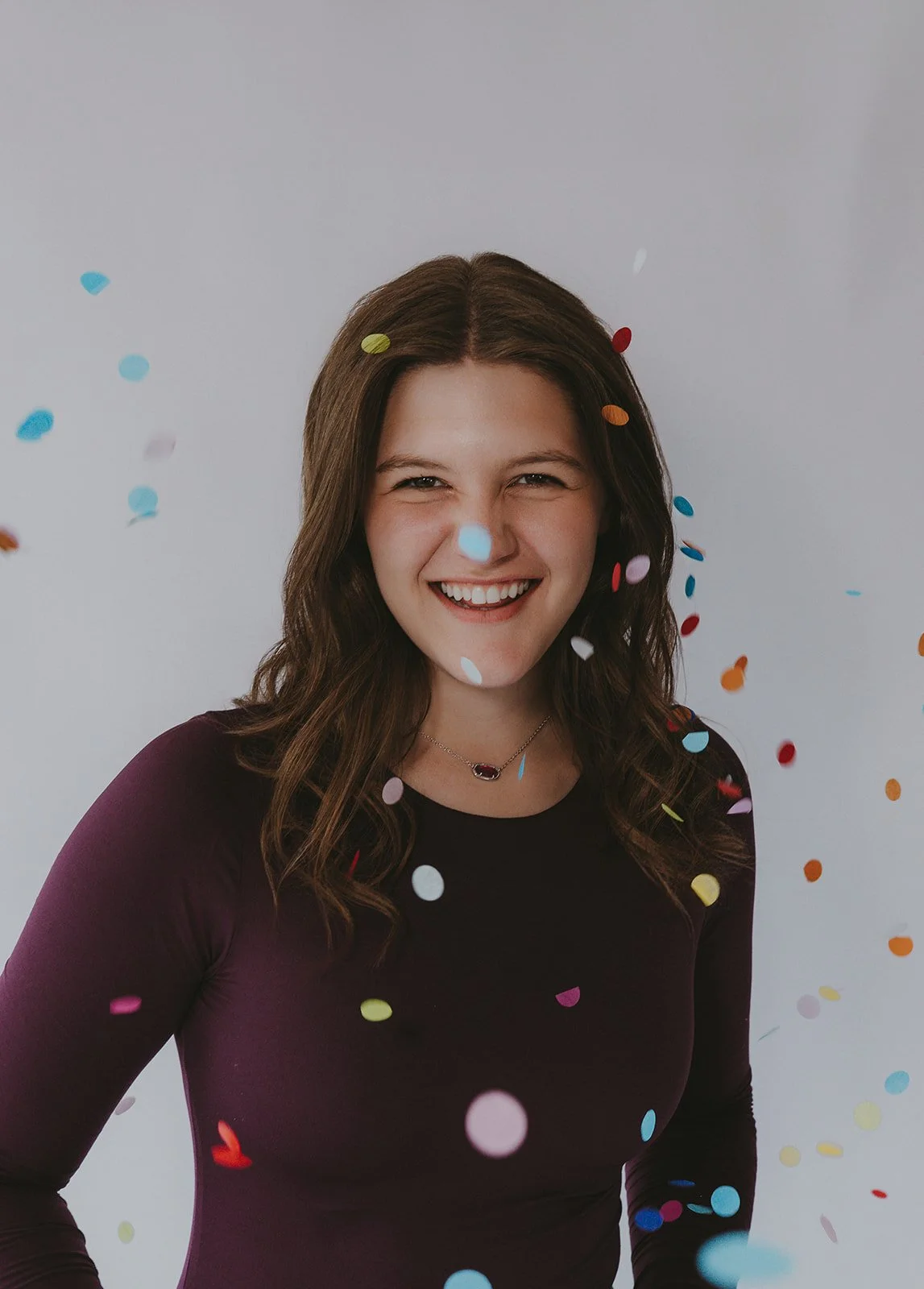 Woman in a purple top smiling in a swirl of confetti.