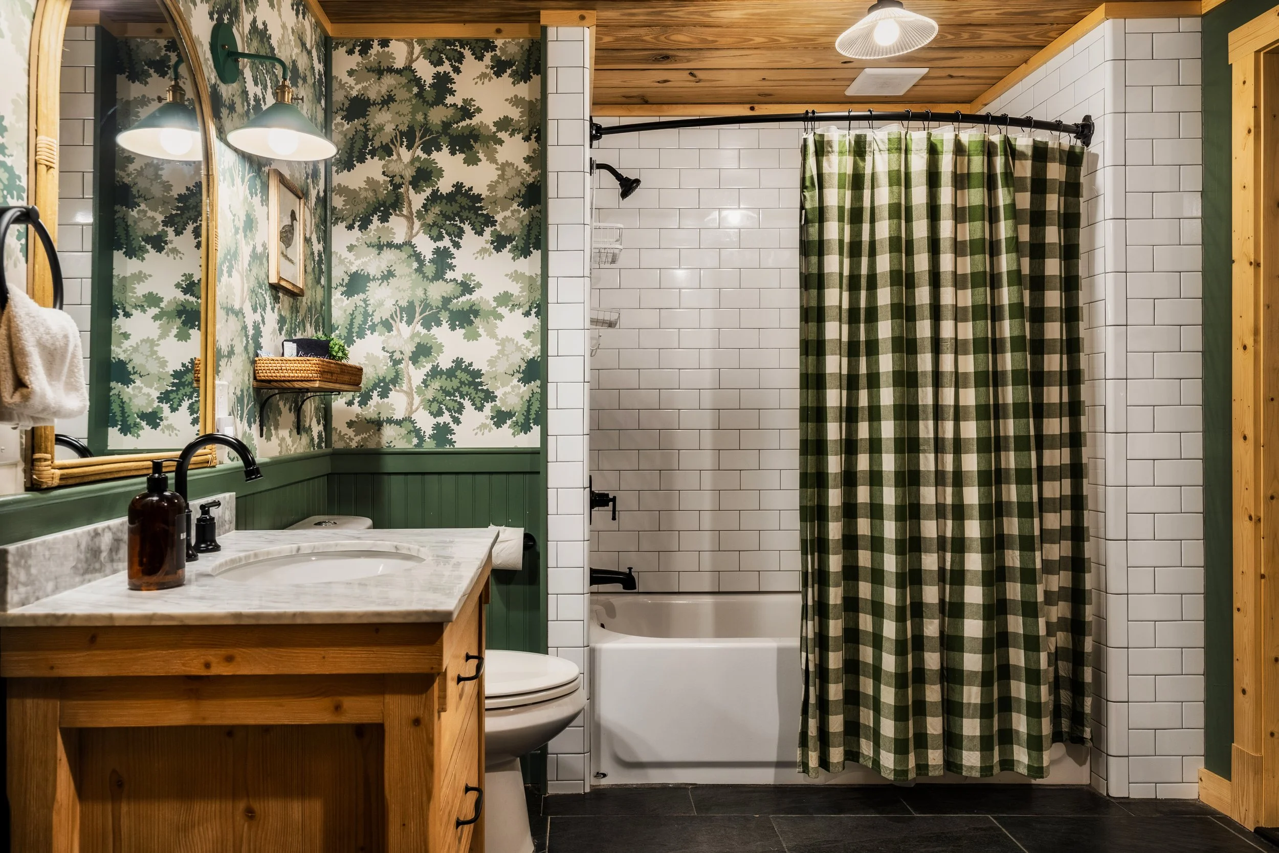 Bathroom with green and white checkered shower curtain, white subway tile walls, wooden ceiling, patterned wallpaper, marble sink, and wooden vanity.