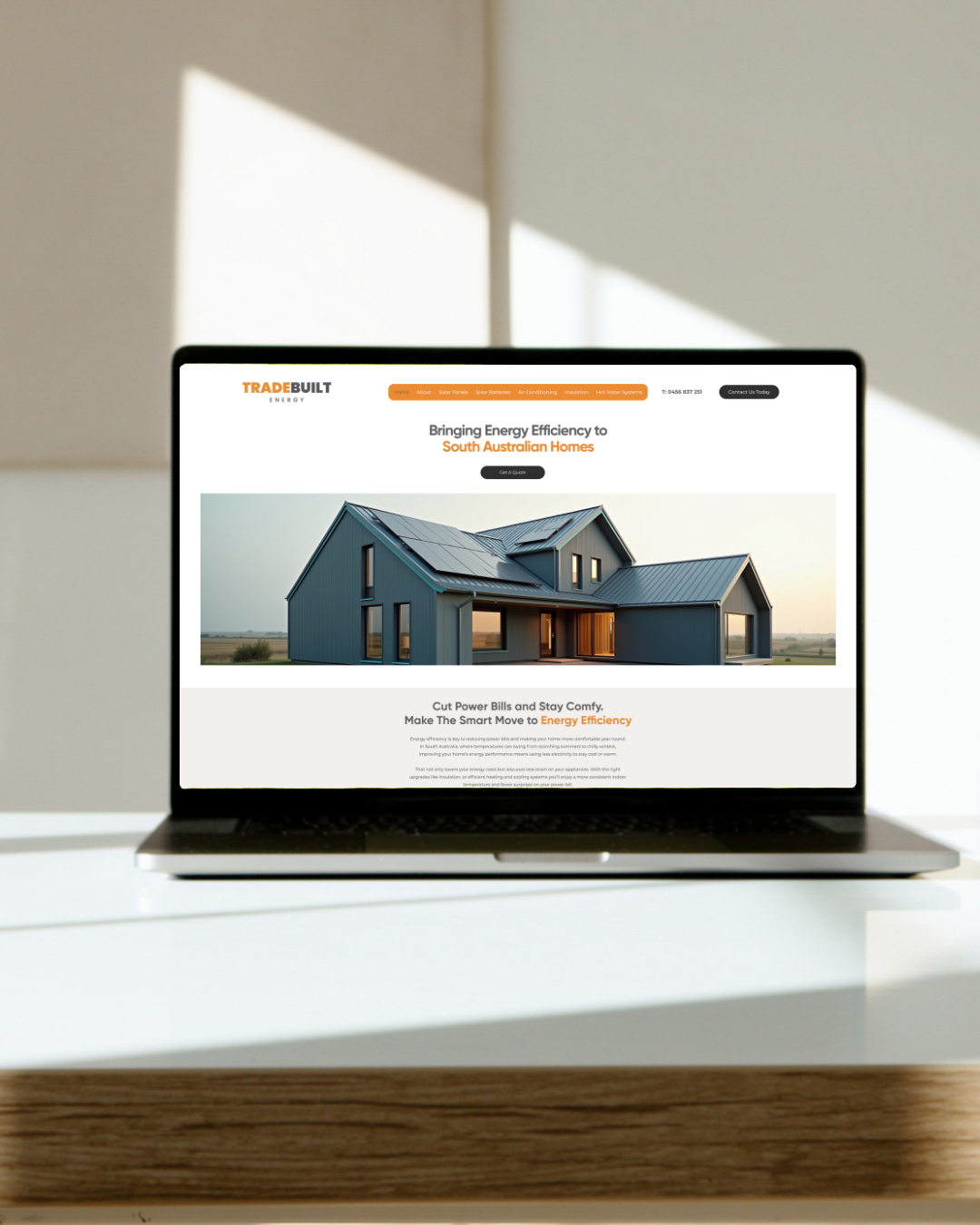 Laptop on a white desk displaying a website about energy efficiency for South Australian homes, with a modern house and solar panels on the screen.