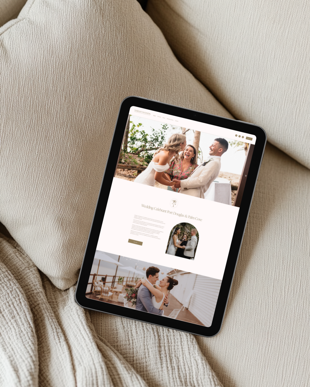 Tablet showing a wedding website with images of a couple and a wedding ceremony, resting on a beige sofa.