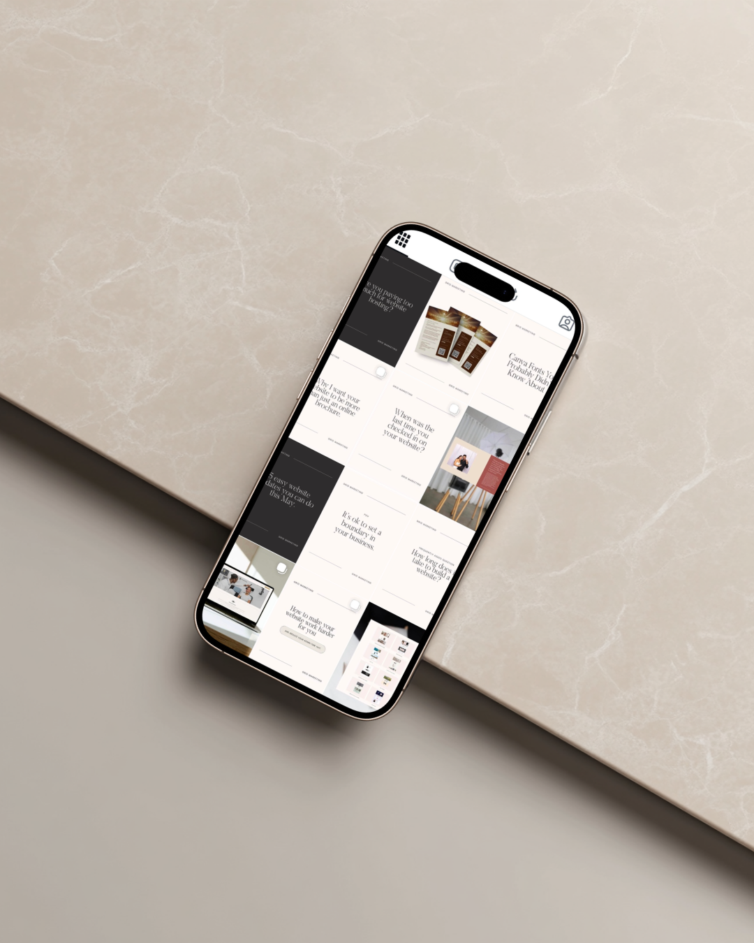 Smartphone displaying a grid of social media or website post previews, resting on a beige marble surface.