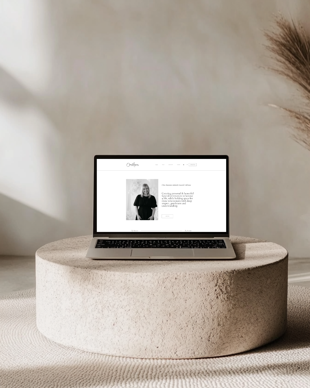 Laptop displaying a website with a photo of a woman, placed on a textured circular platform in a minimalistic room.
