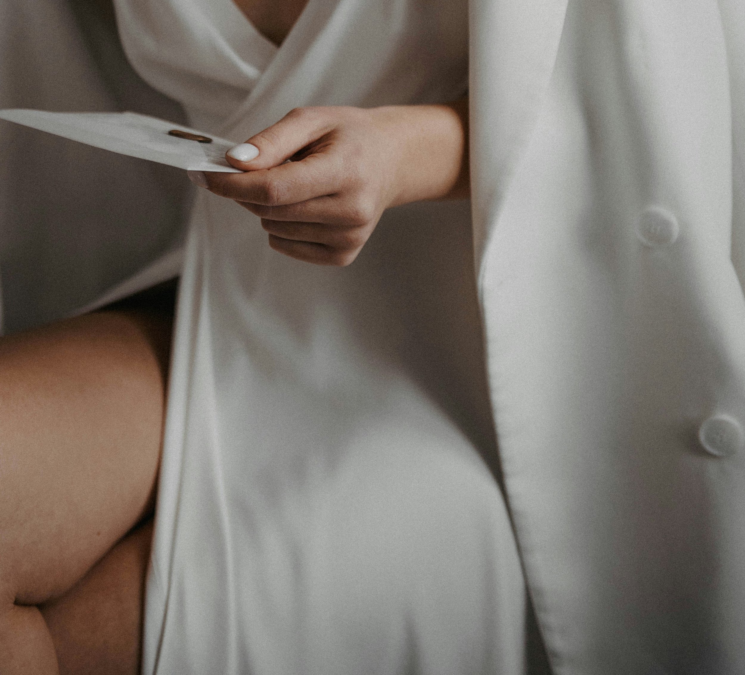 Close-up of a hand with white painted nails holding a small card or paper near a white buttoned garment.