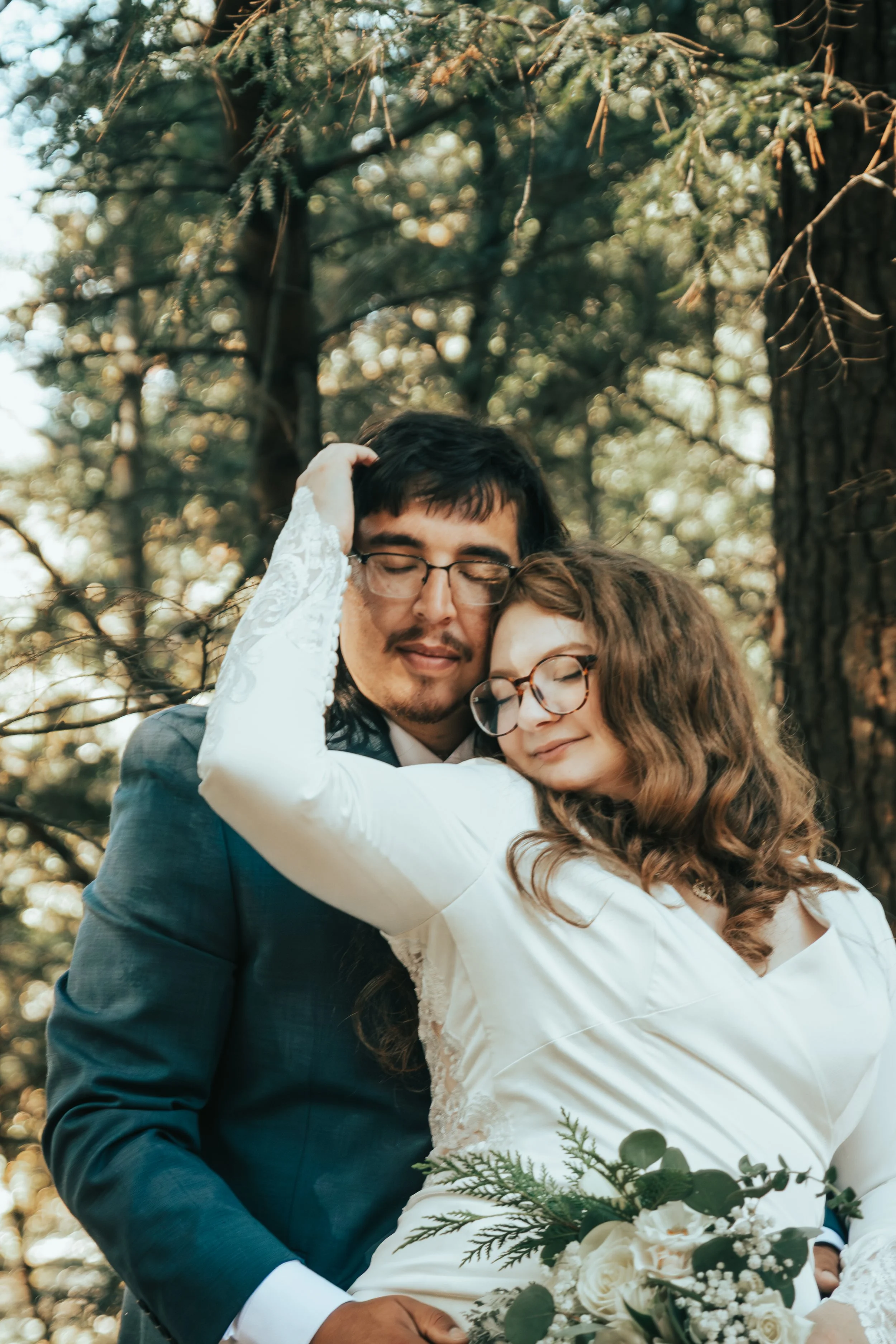 Red Cliff tribal couple embracing outdoors during their wedding day, captured in natural light among trees, highlighting their connection.