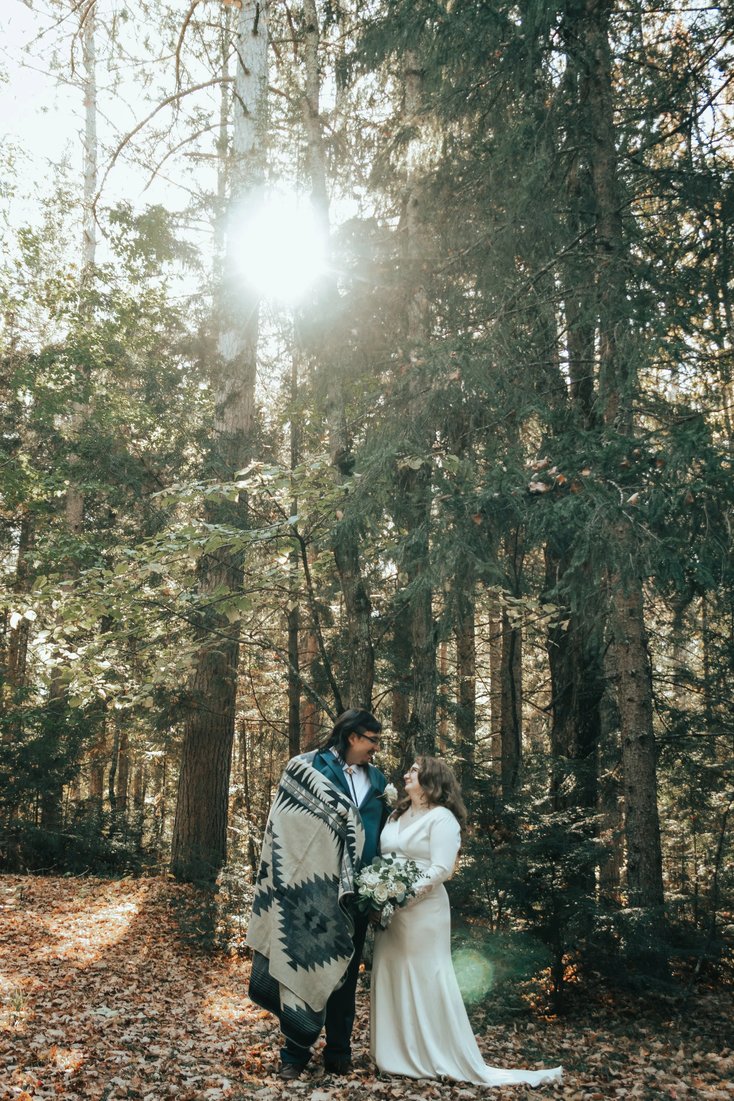 Red Cliff tribal couple on their wedding day in a forest, sharing a quiet, candid moment, with sunlight filtering through tall trees.