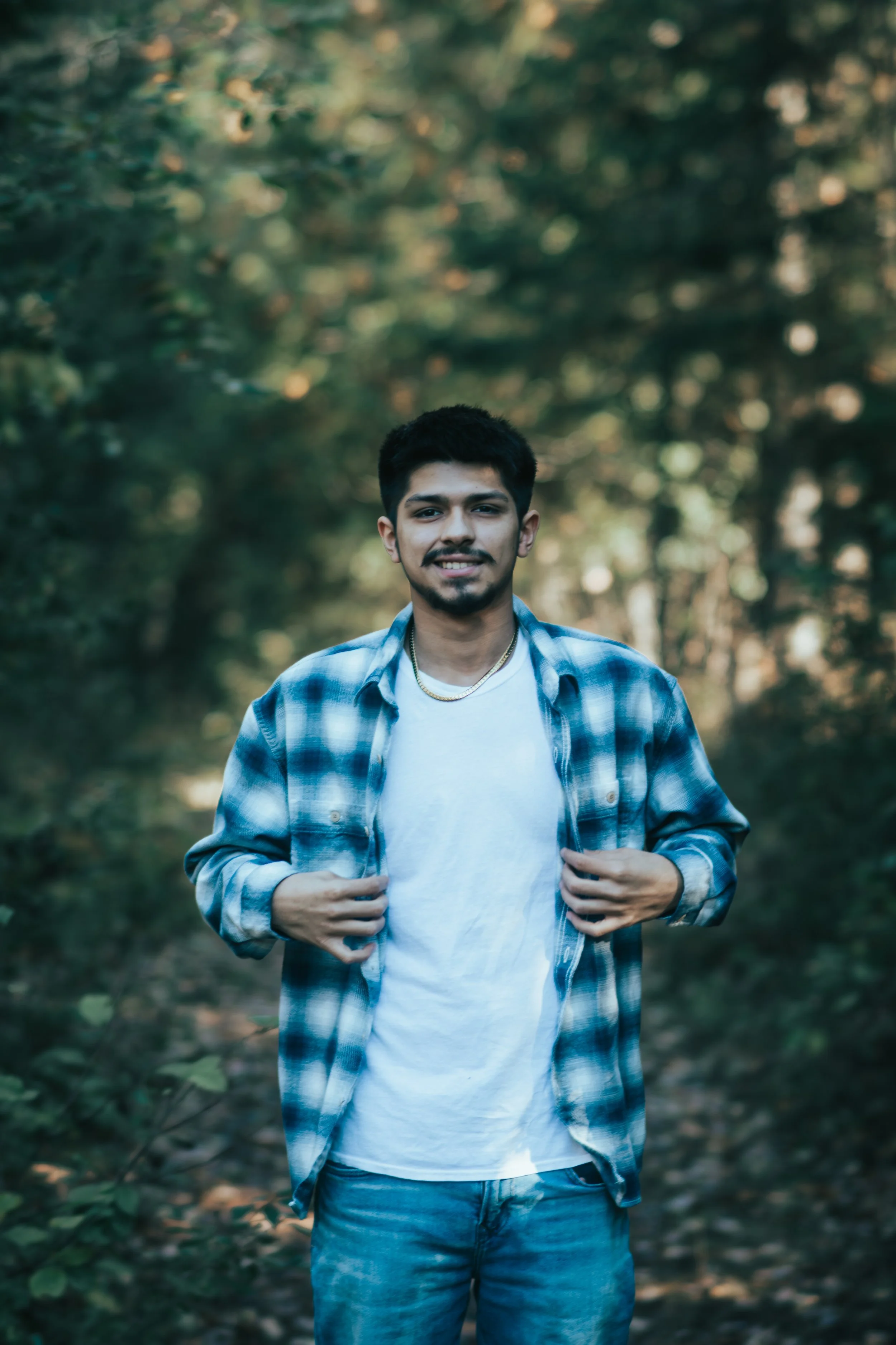 Senior portrait of a Bad River young man smiling in a forest setting, captured with natural light and candid style.