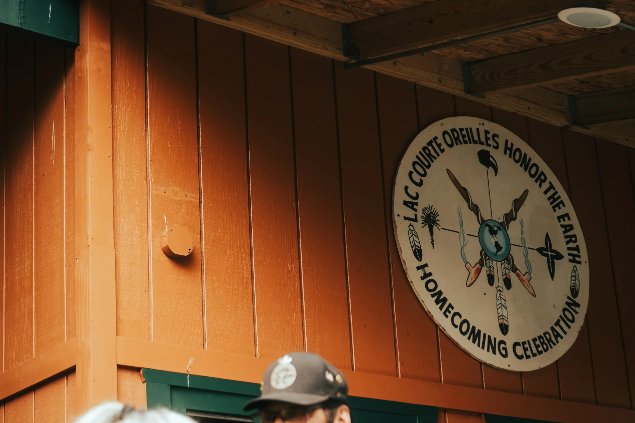 Close-up of a sign at the Lac Courte Oreilles Honor the Earth Homecoming Celebration, featuring feather, arrow, and bird symbols, representing a Native community event.