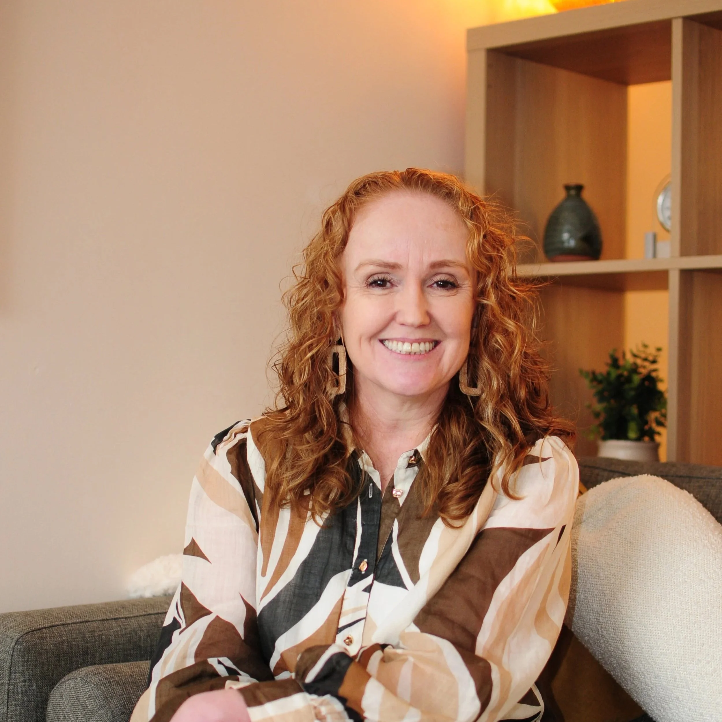 Elissa. woman with red curly hair sitting crossed legged and smiling