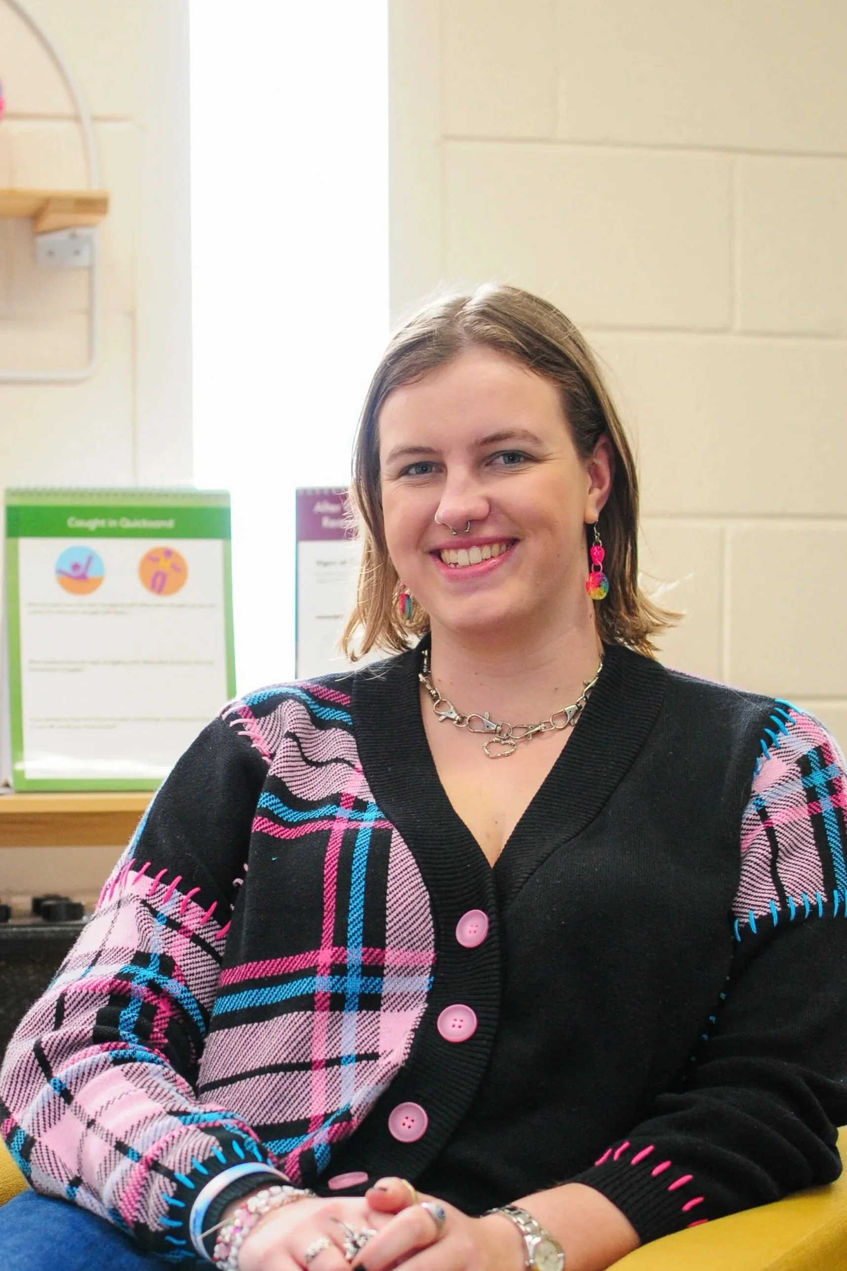 woman smiling with septum piercing and rainbow earrings and medium length brown hair 