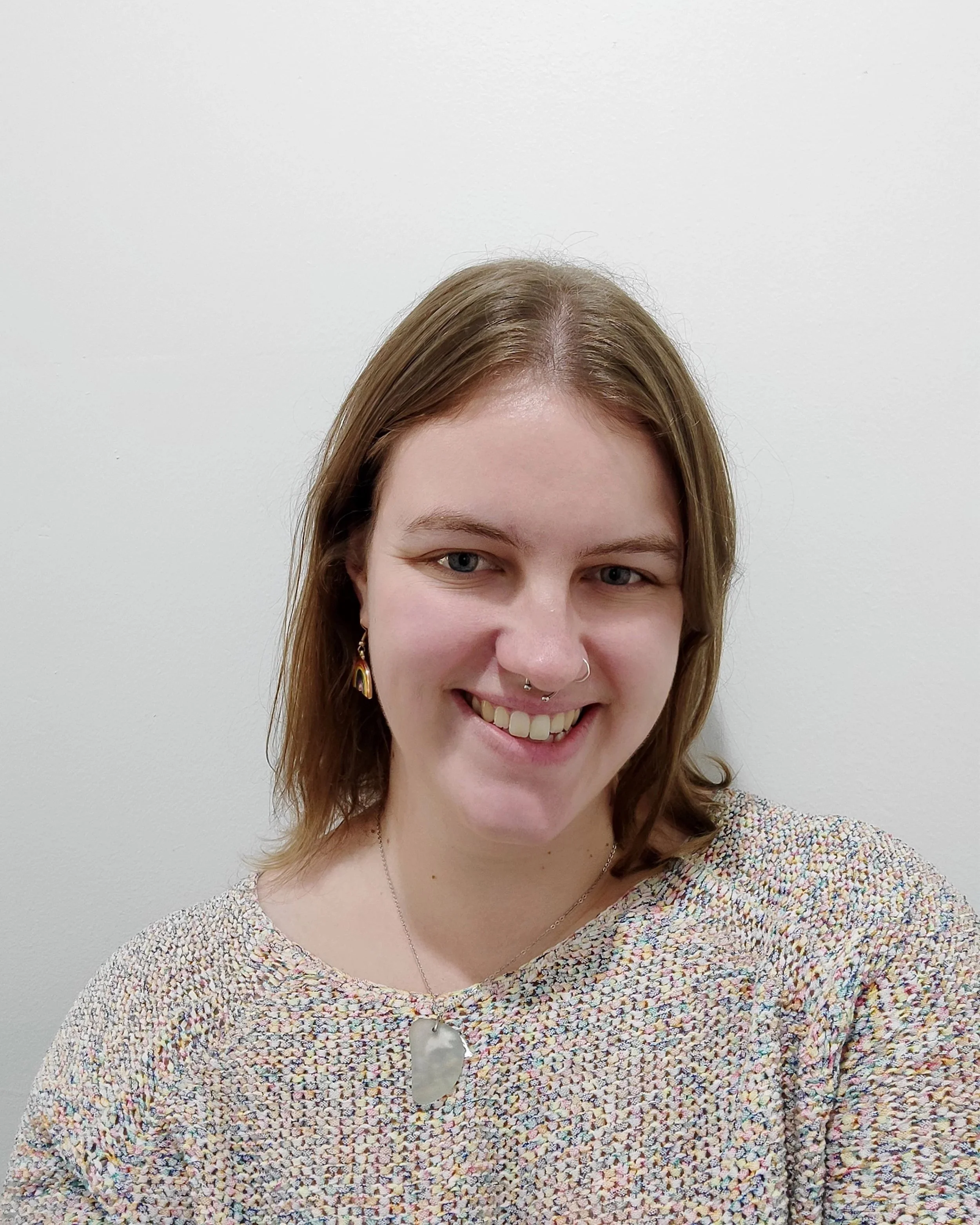 woman smiling with septum piercing and rainbow earrings and medium length brown hair