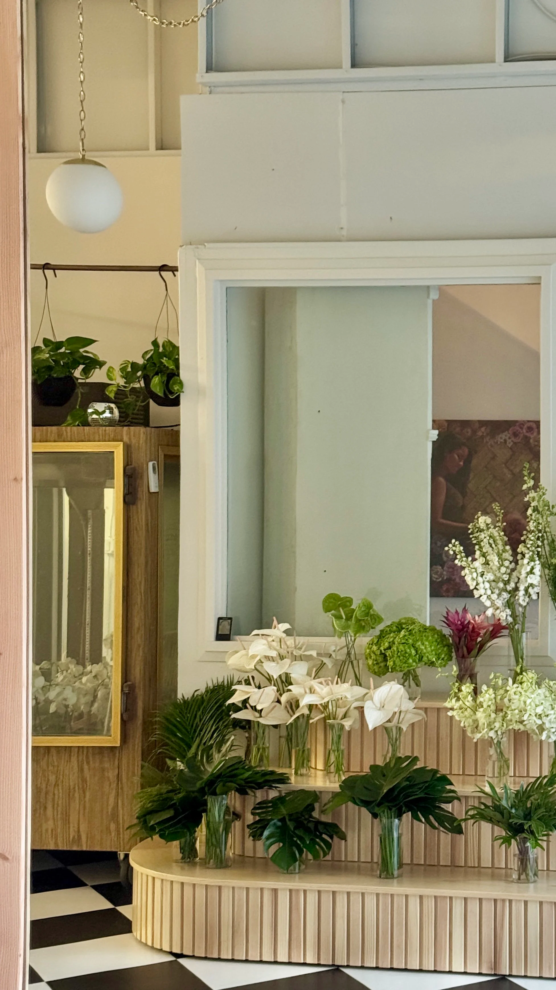 Indoor space with display of various white and green flowers in vases, a mirror, and a black and white checkered floor.