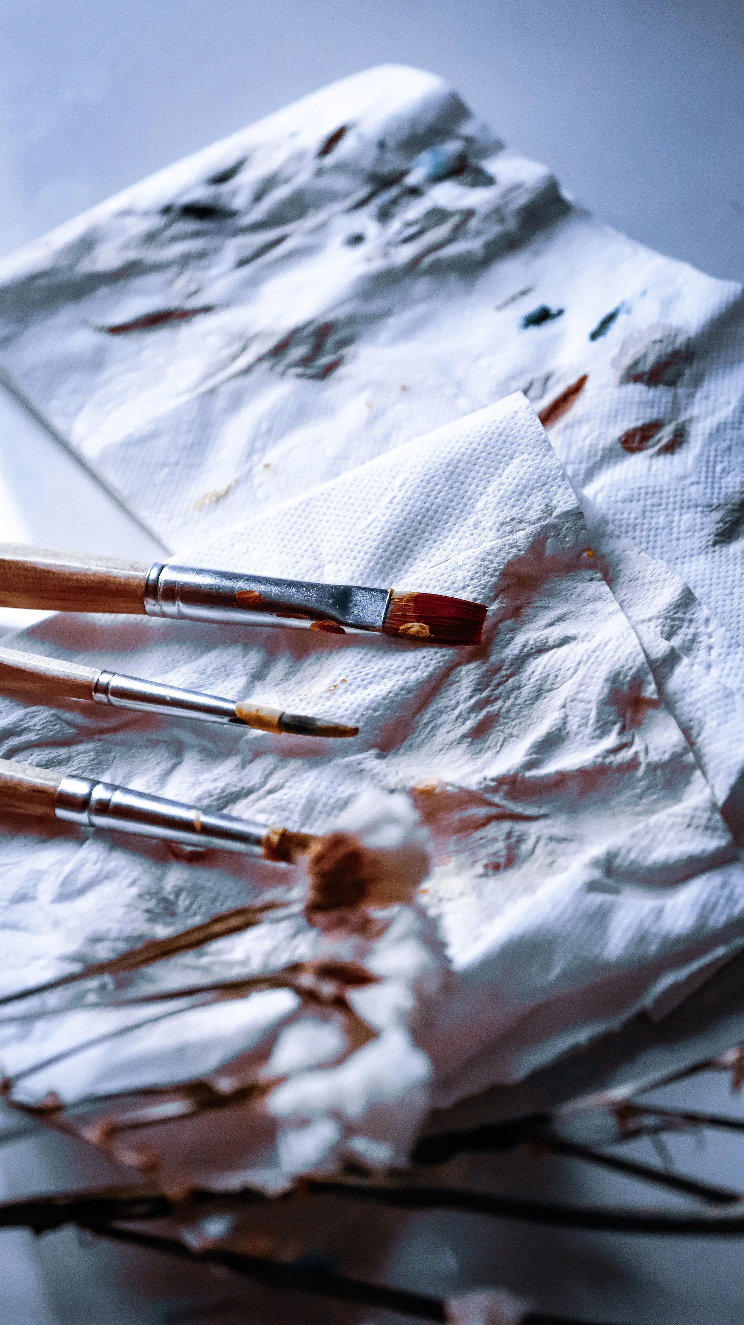 Paintbrushes resting on crumpled tissue paper with paint stains, possibly an art workspace.