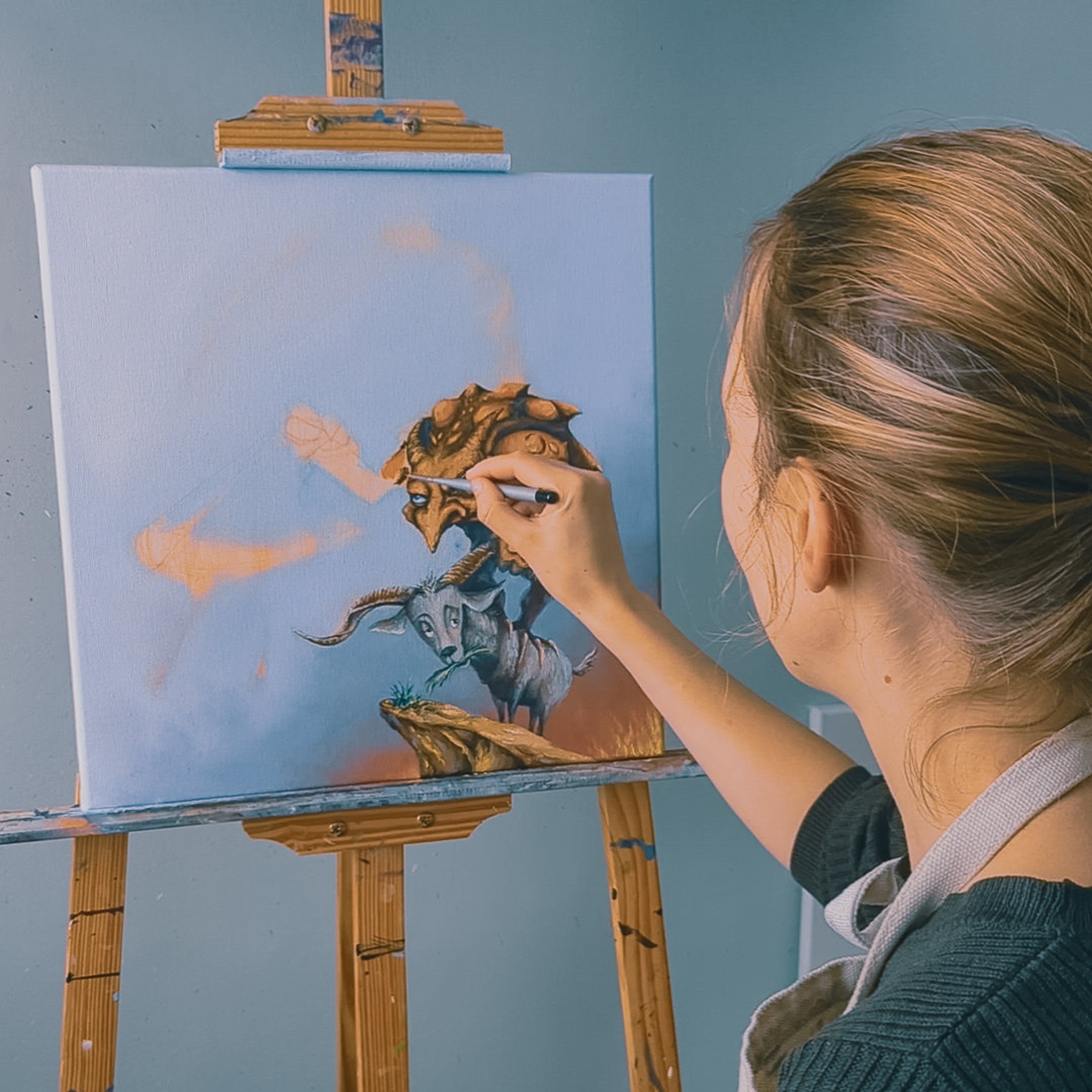 Person painting a fantasy creature on canvas with a wooden easel