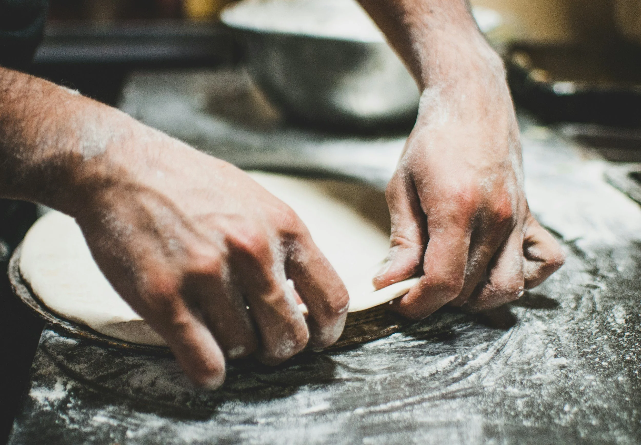 a close up of a person handling a sourdough pizza dough on a floured surface