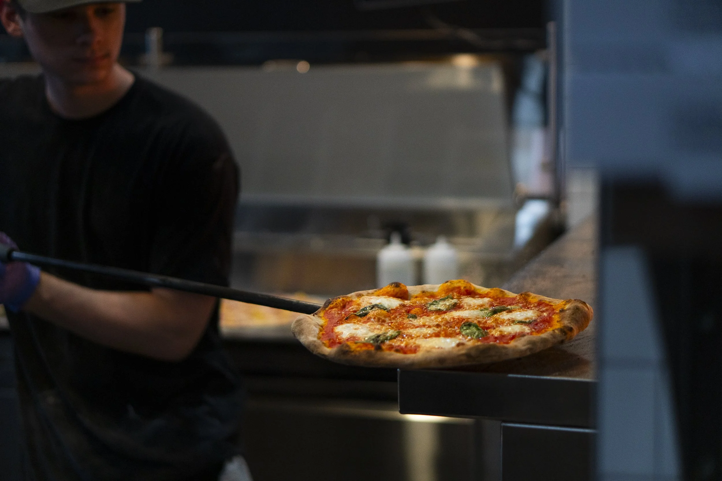 Close‑up of freshly baked sourdough pizza crust showing natural blistering, golden caramelization, and airy, open crumb texture.