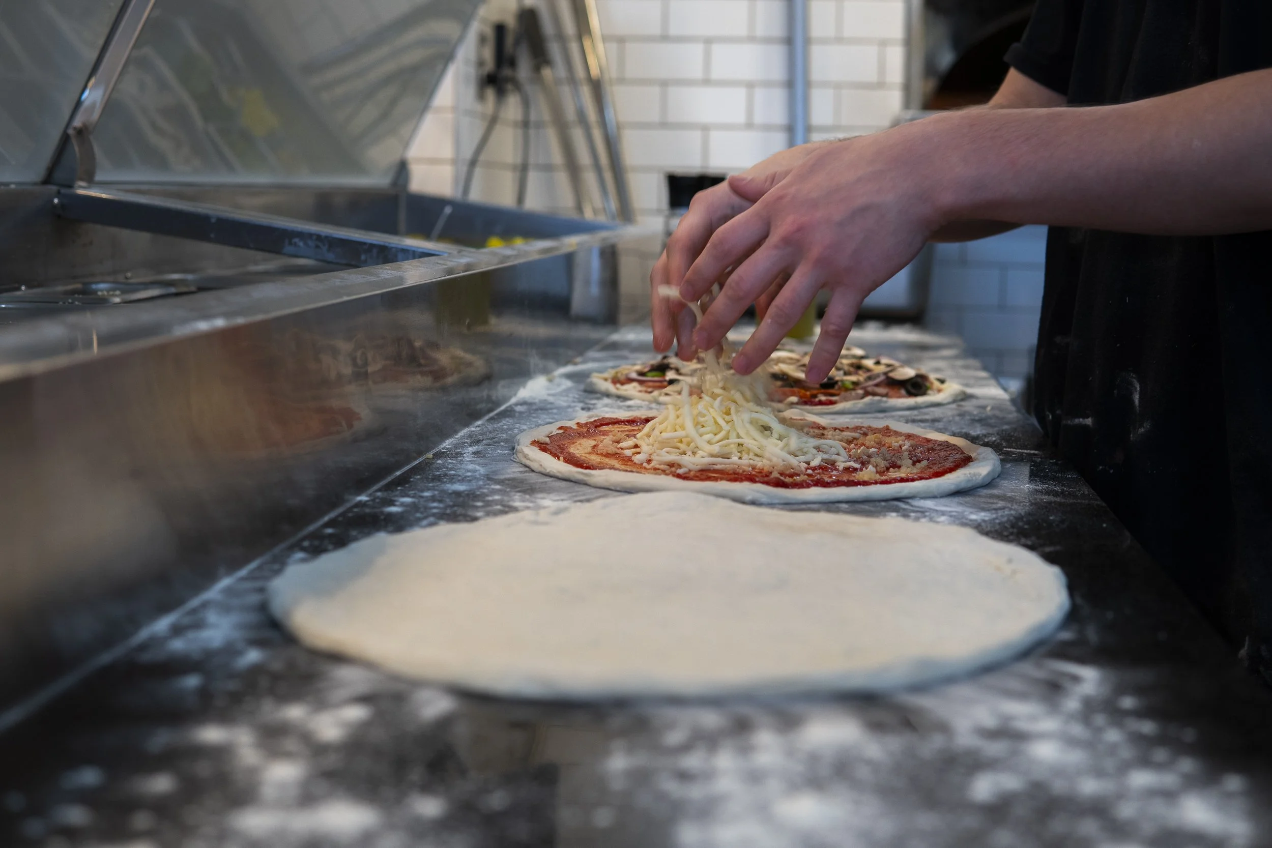 a line of sourdough pizza doughs being topped for cooking