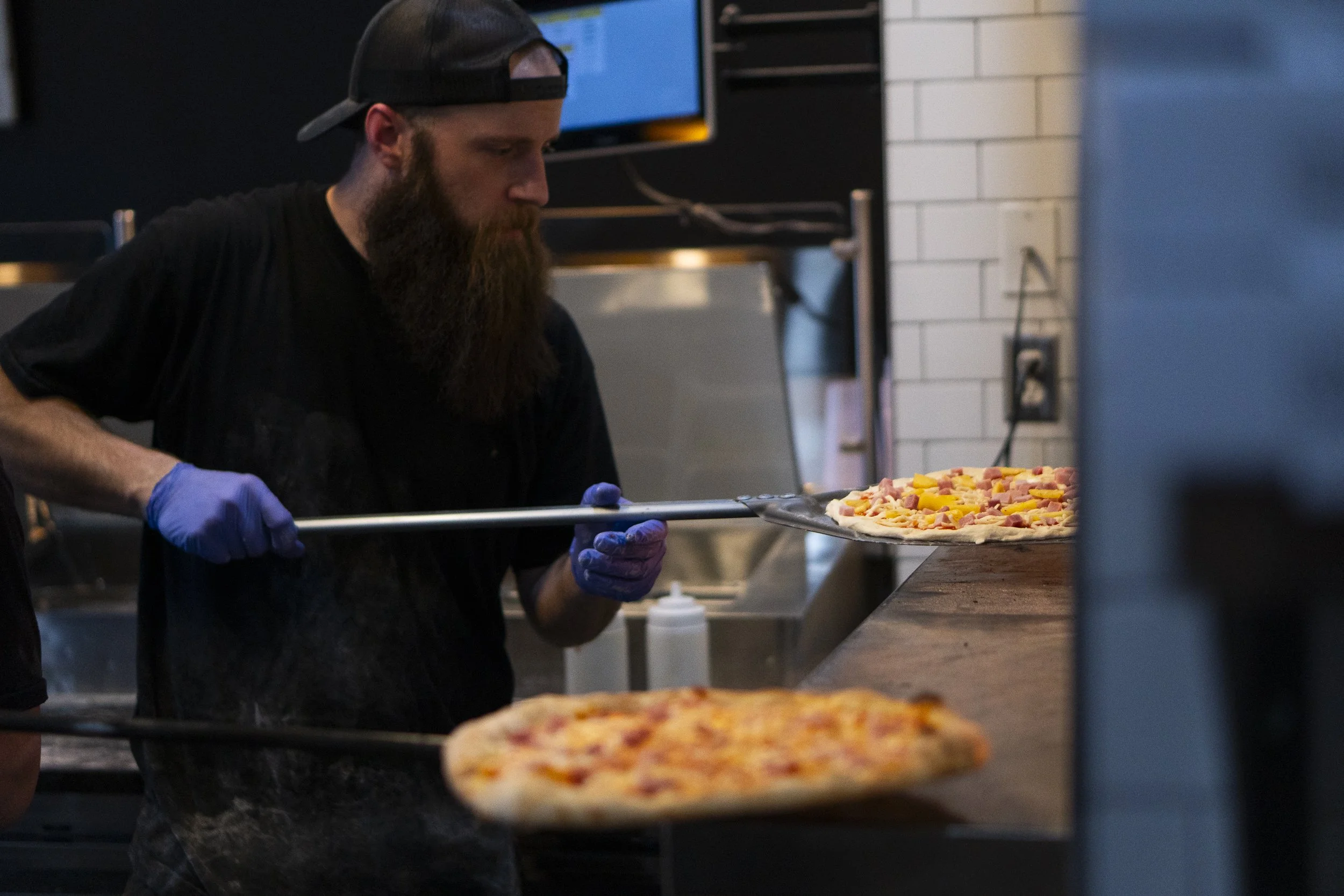 a sourdough pizza company employee places a fresh sourdough pizza in the oven