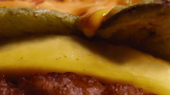 a close up of a hamburger with cheese and pickles.gif