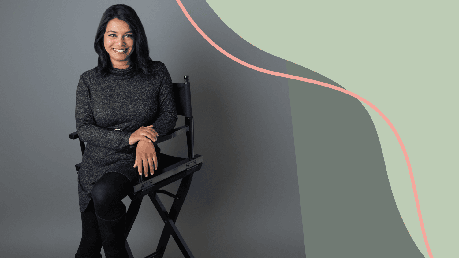 Kavita Sienknecht sits on a director's chair smiling in a black outfit