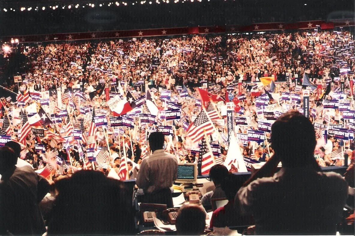 A large political rally with many people holding American flags and campaign signs supporting George W. Bush.
