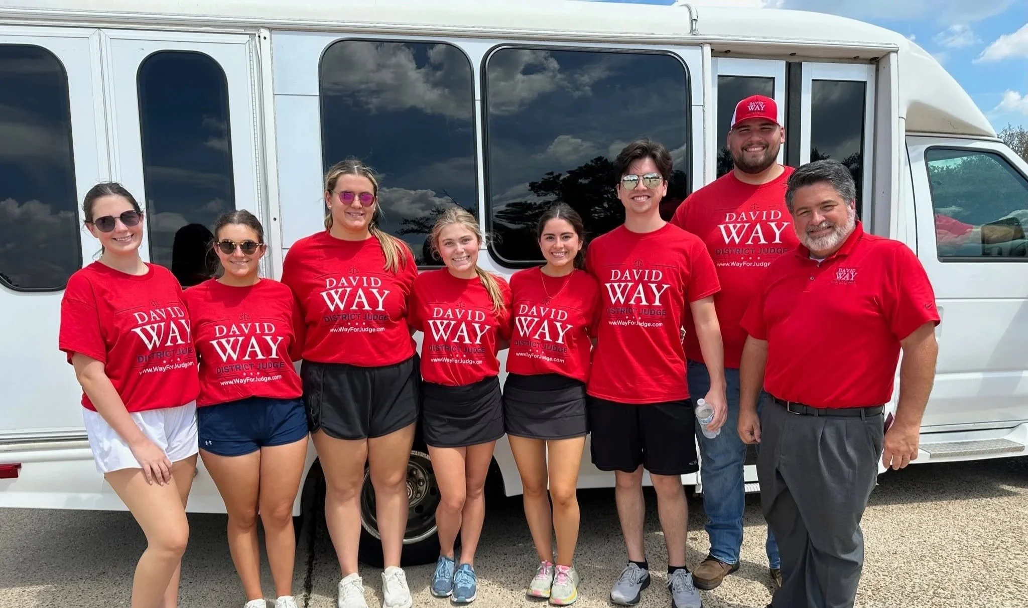 Group of Way-Walkers standing in front of a large white bus, all wearing red shirts that say 'David Way District Judge'.