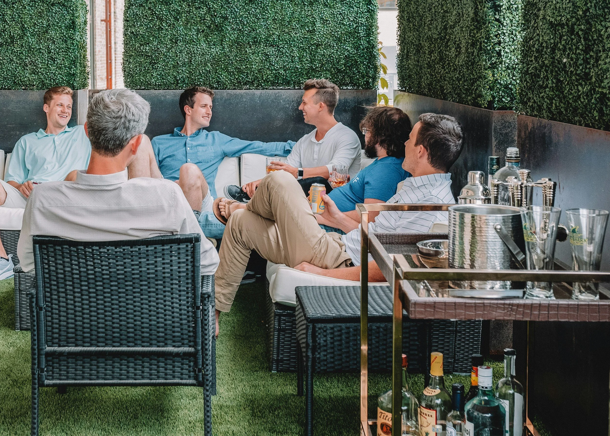 Group of friends sitting together on an outdoor patio, socializing and enjoying drinks, with a bar cart in the foreground.