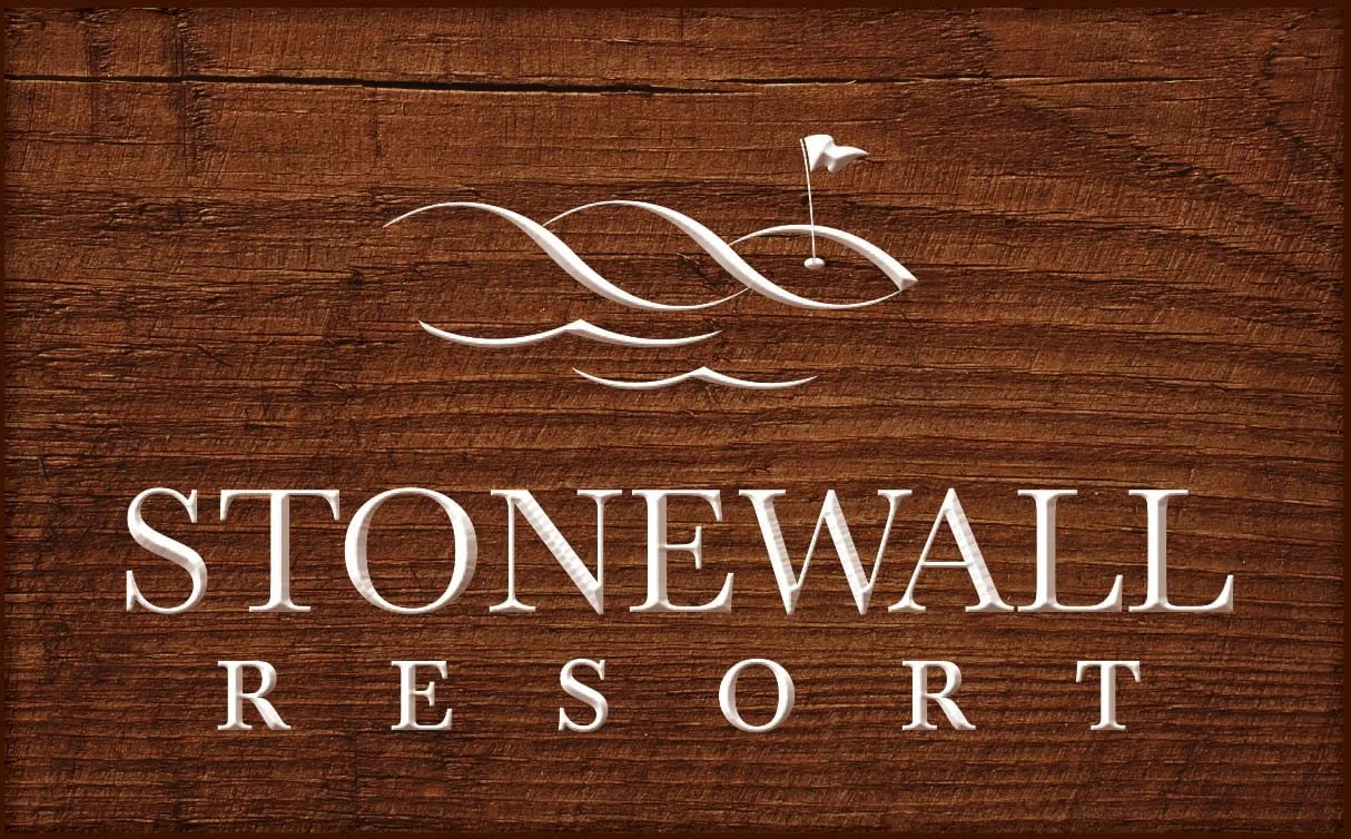 Wooden sign with a white stylized sailboat above the words "Stonewall Resort" in large white letters, on a wood-textured background.