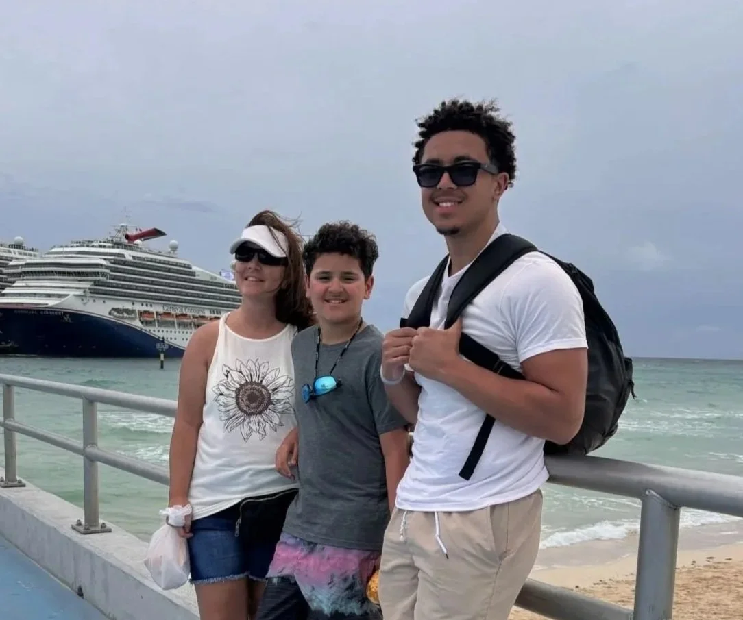 Nicole with her two sons on their latest vacation to the Bahamas. They are standing on a cruise ship pier with the bright blue ocean behind them.