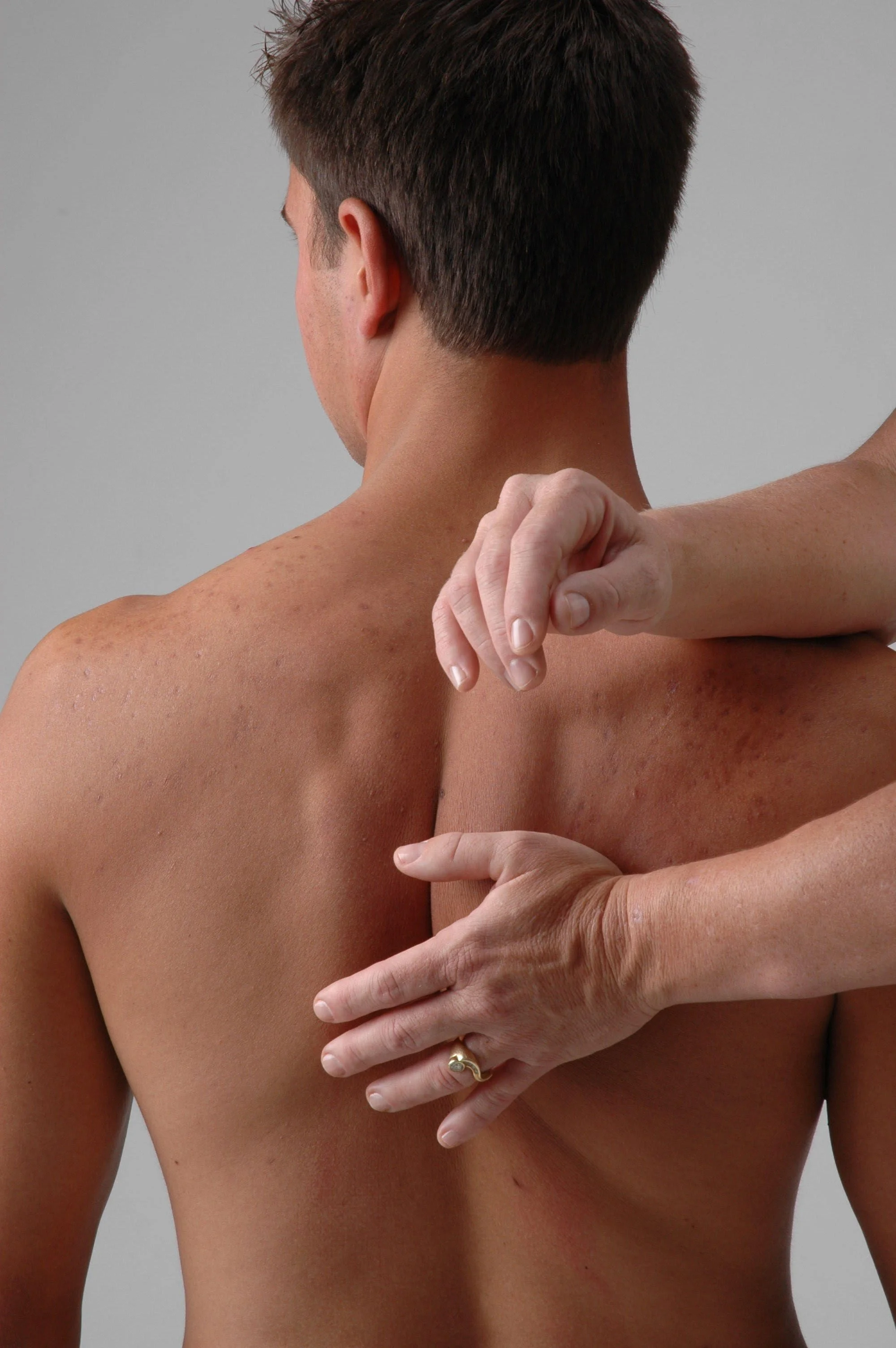 A man's bare back with his head turned to the side, two hands from a Rolfing Practitioner are manipulating his back