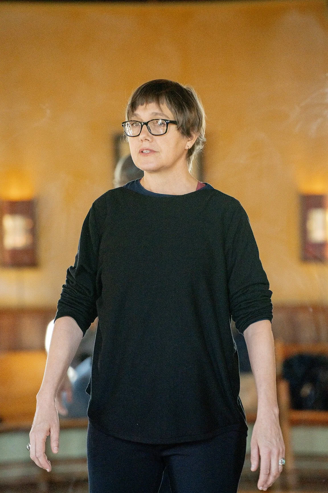Liesje Smith, with short brown hair, glasses, and wearing a black sweater, sleeves rolled up, walking through a movement studio, teaching a RolfMovement LAB.