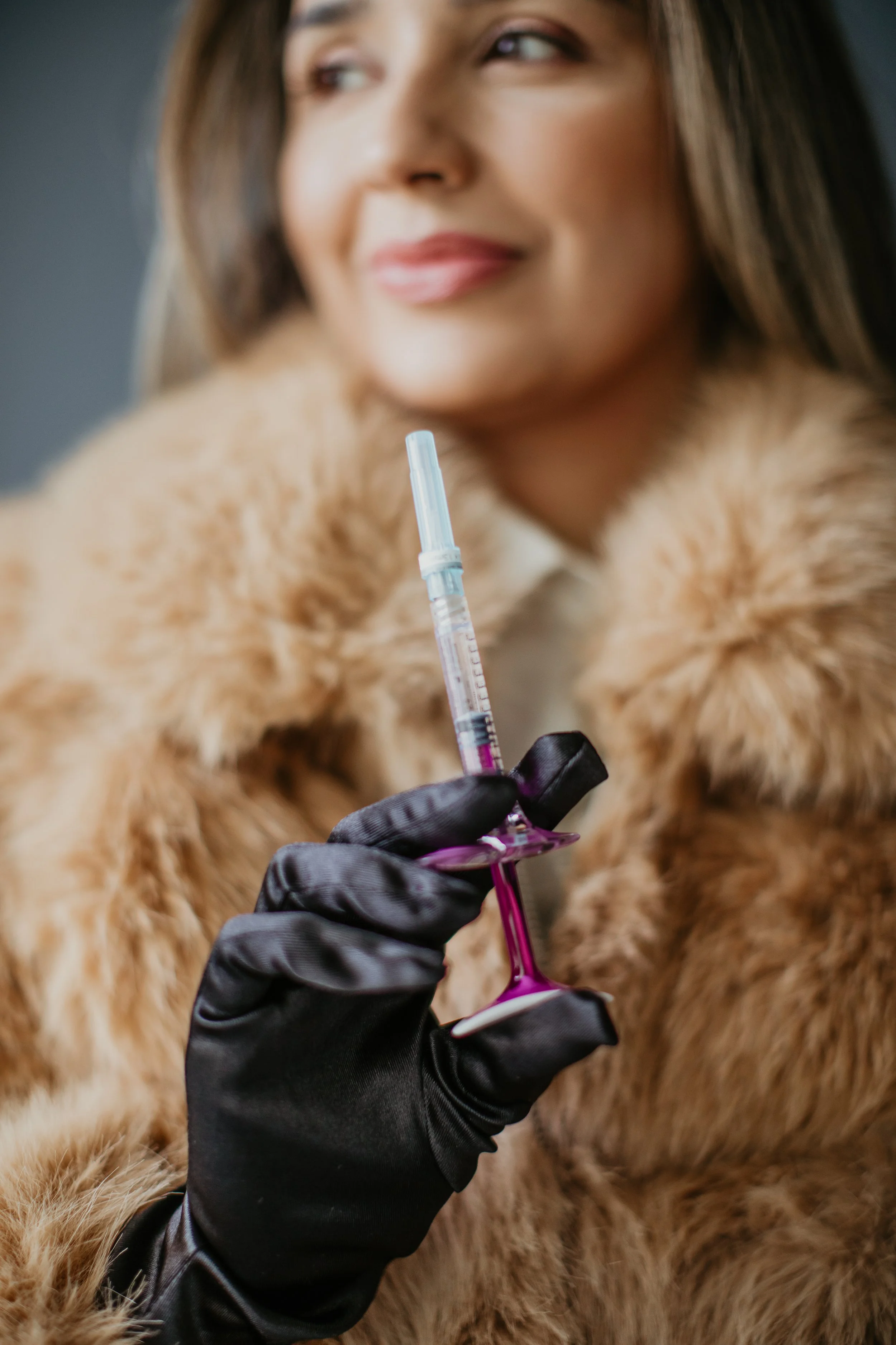Gloved hand holding a dermal filler syringe with Simi Kennedy ARNP smiling in the background at Sona Medical Aesthetics Newcastle WA