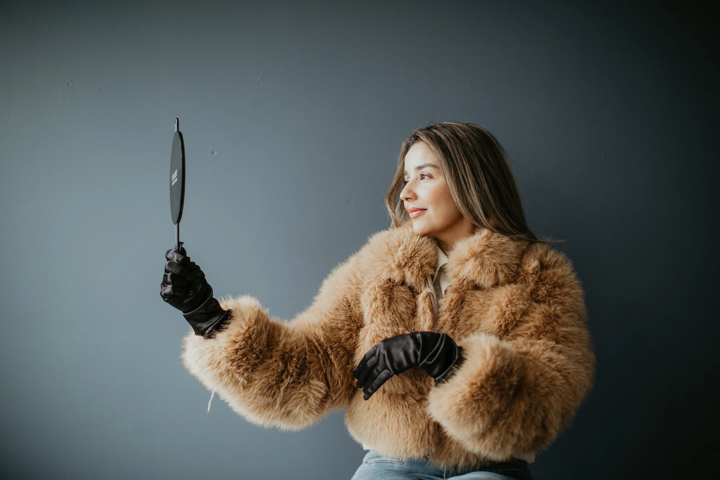 Simi Kennedy ARNP wearing black gloves and holding a Daxxify mirror in a brand lifestyle photo at Sona Medical Aesthetics Newcastle WA