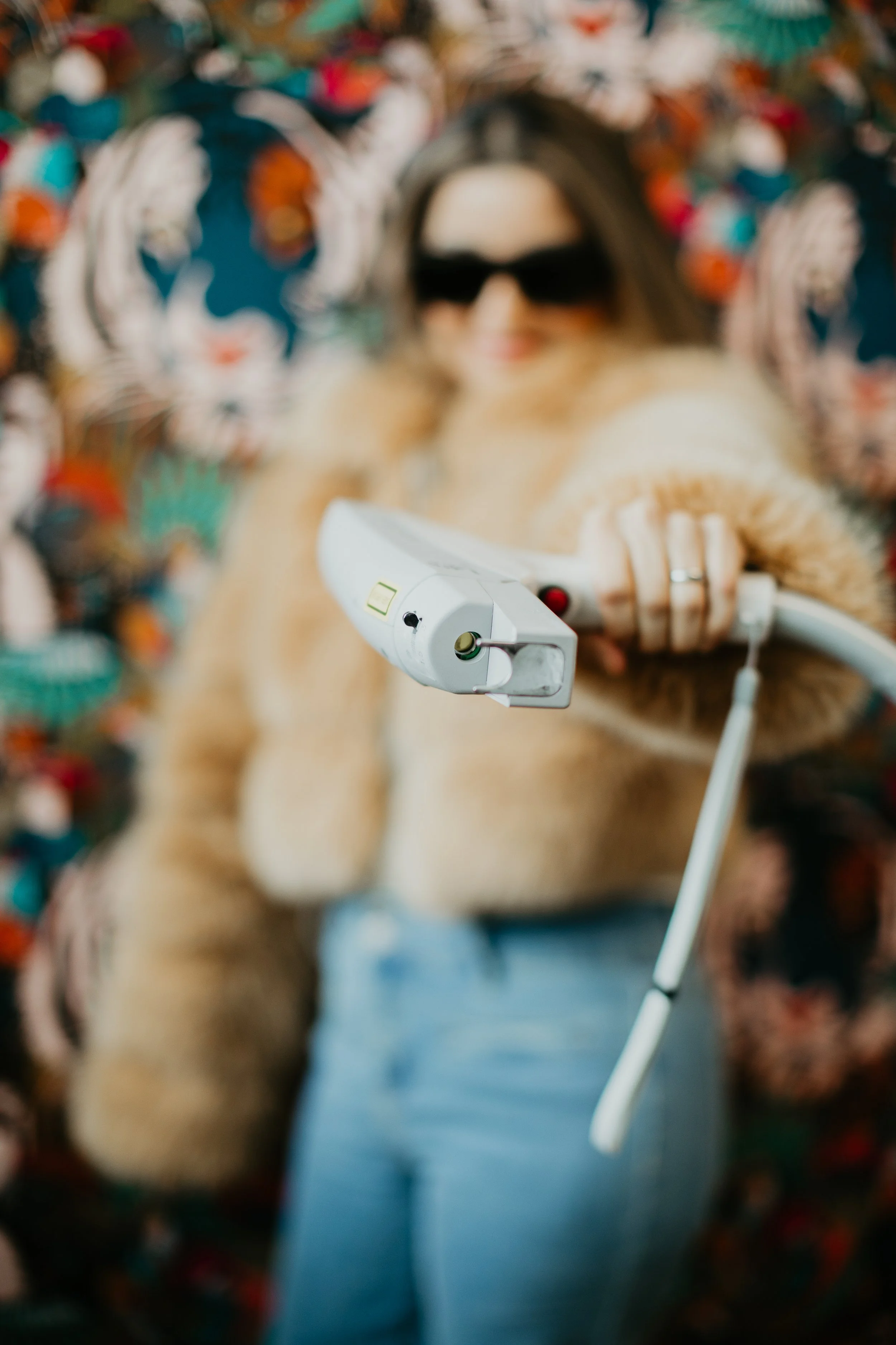 Close-up of a laser treatment handpiece held by a provider in front of Sona Medical Aesthetics signature wallpaper in Newcastle WA