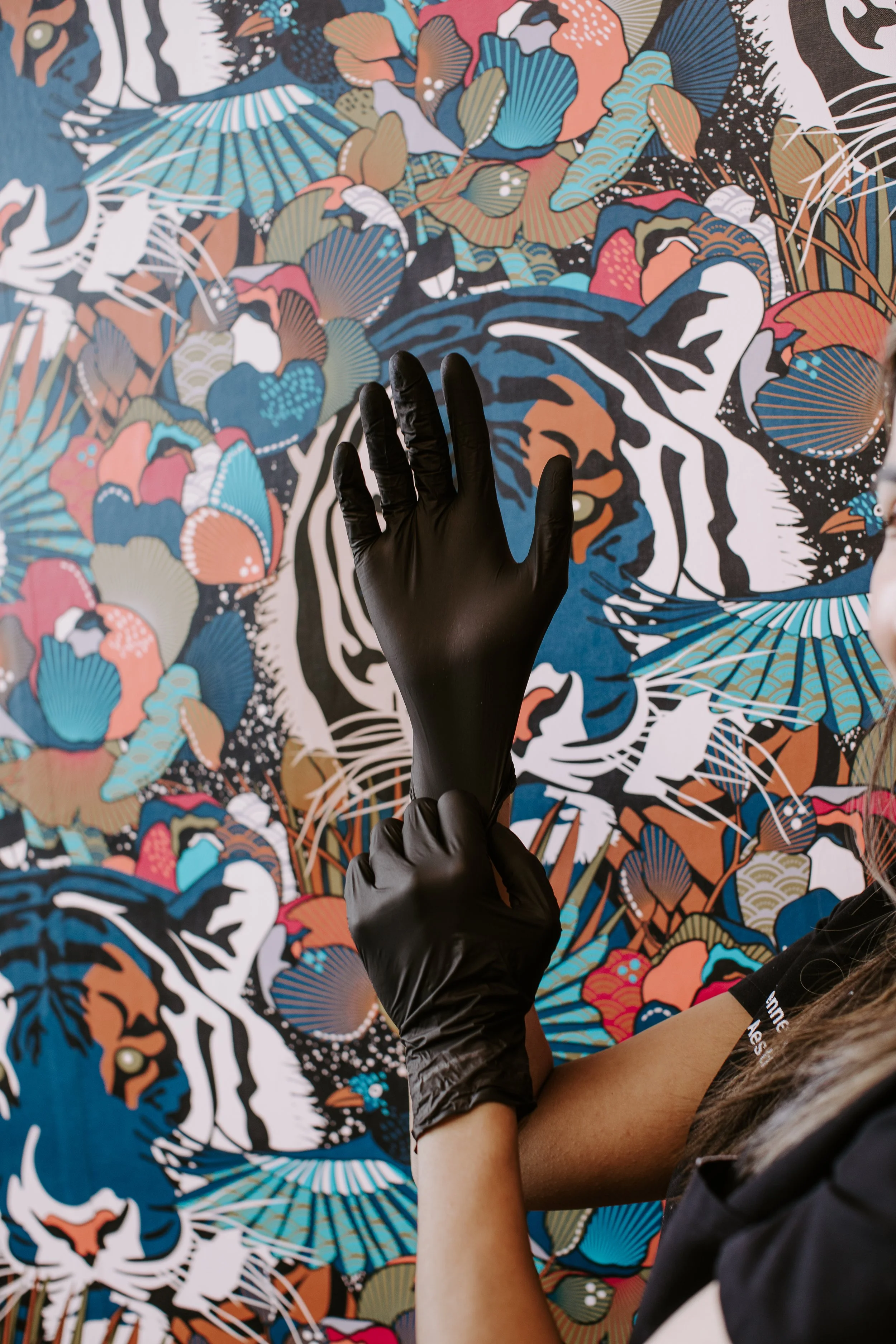 Sona Medical Aesthetics provider putting on black nitrile gloves in front of signature wallpaper at boutique med spa Newcastle WA