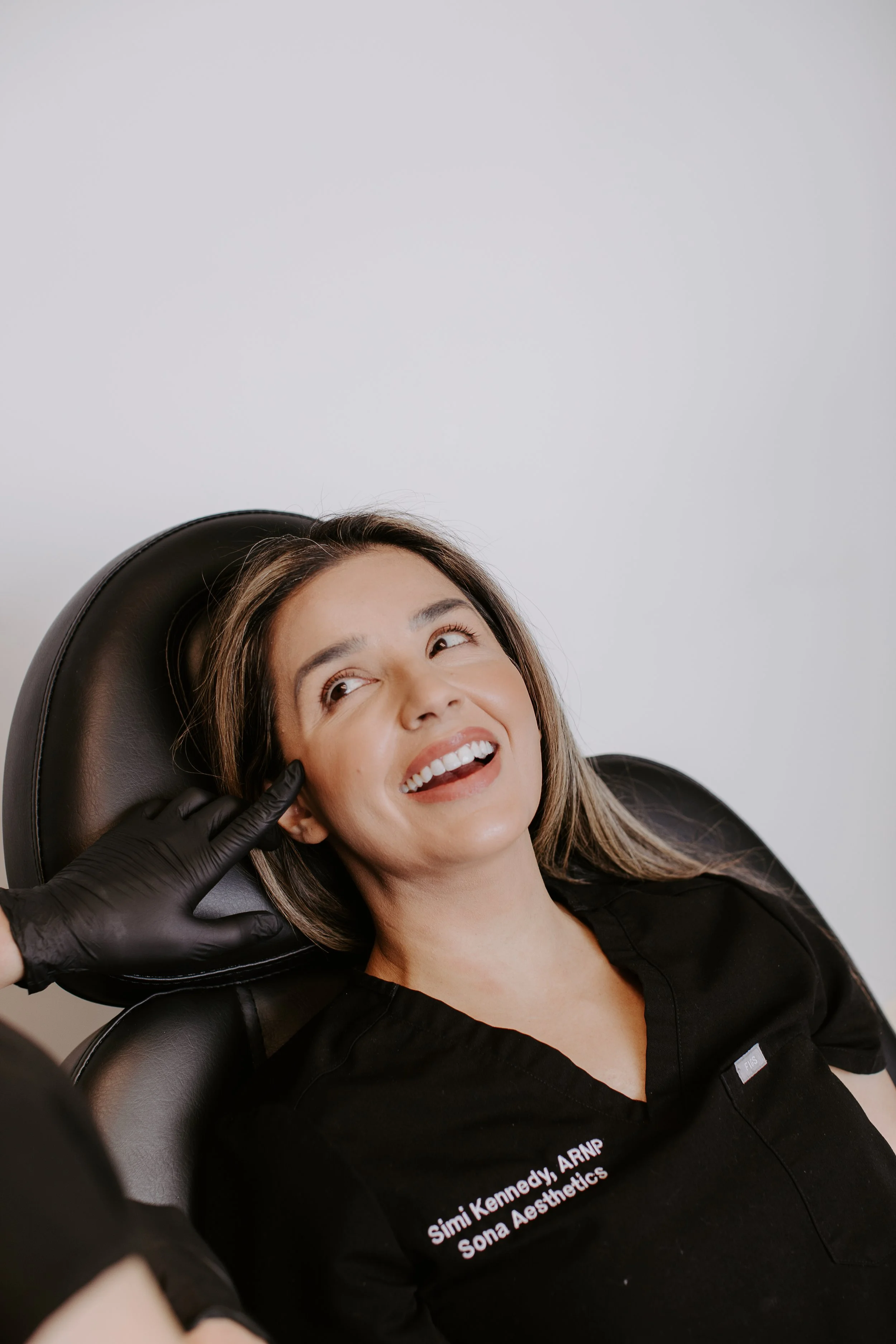 Simi Kennedy ARNP reclined in the treatment chair laughing during a skin treatment at Sona Medical Aesthetics Newcastle WA