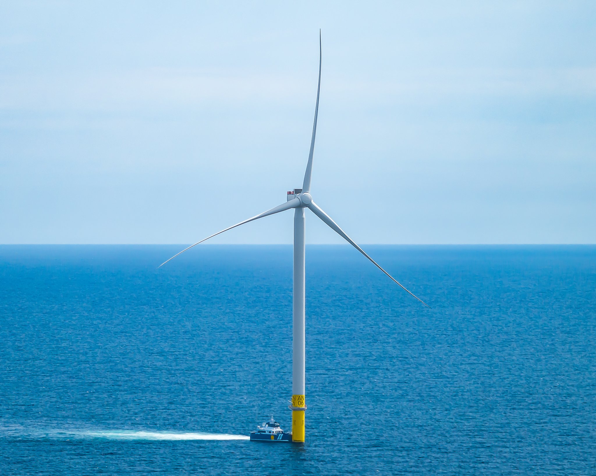 Crew transfer vessel pulled up to the base of a wind turbine, its wake trailing behind.