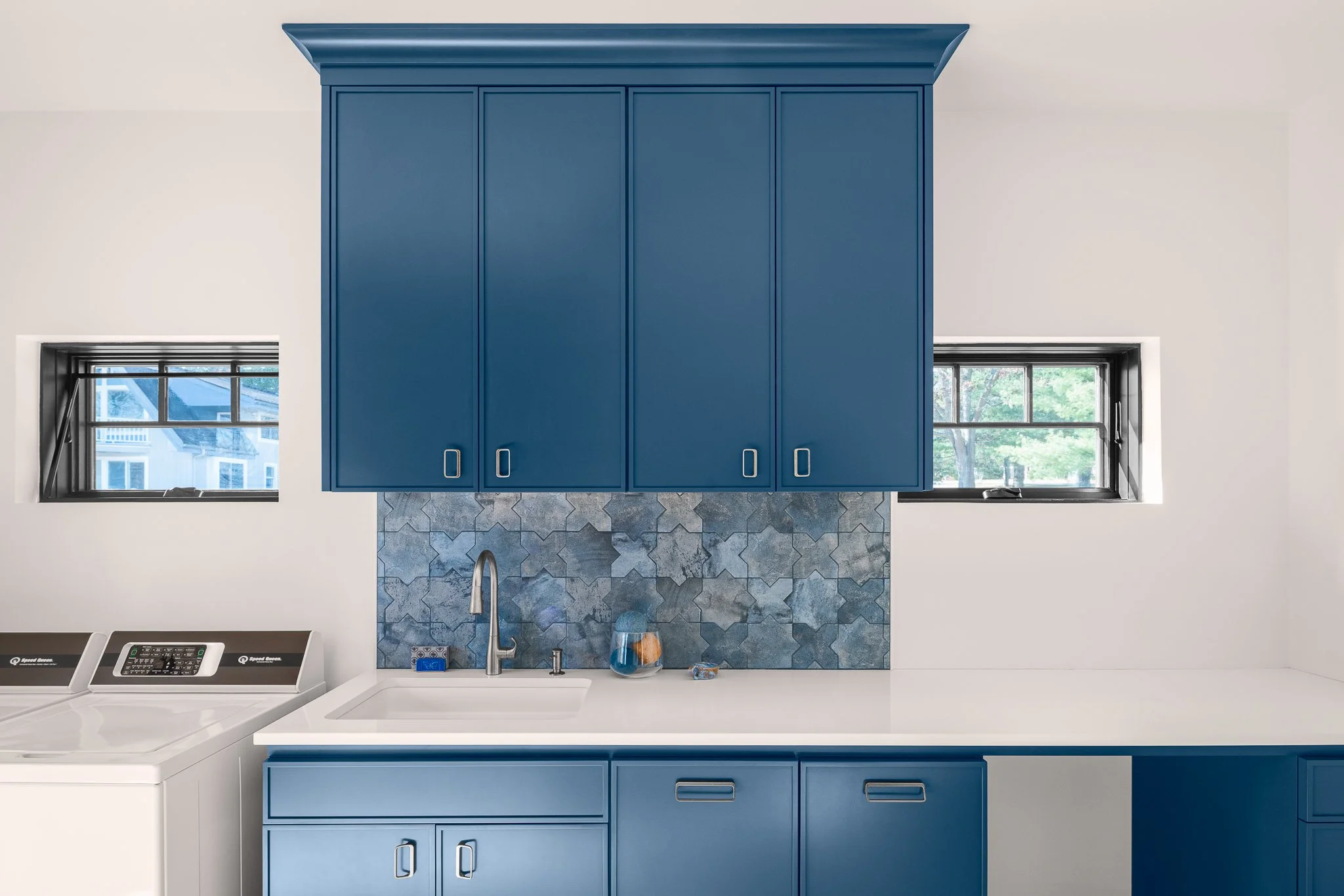 Laundry room with blue upper cabinets and a patterned tile backsplash.