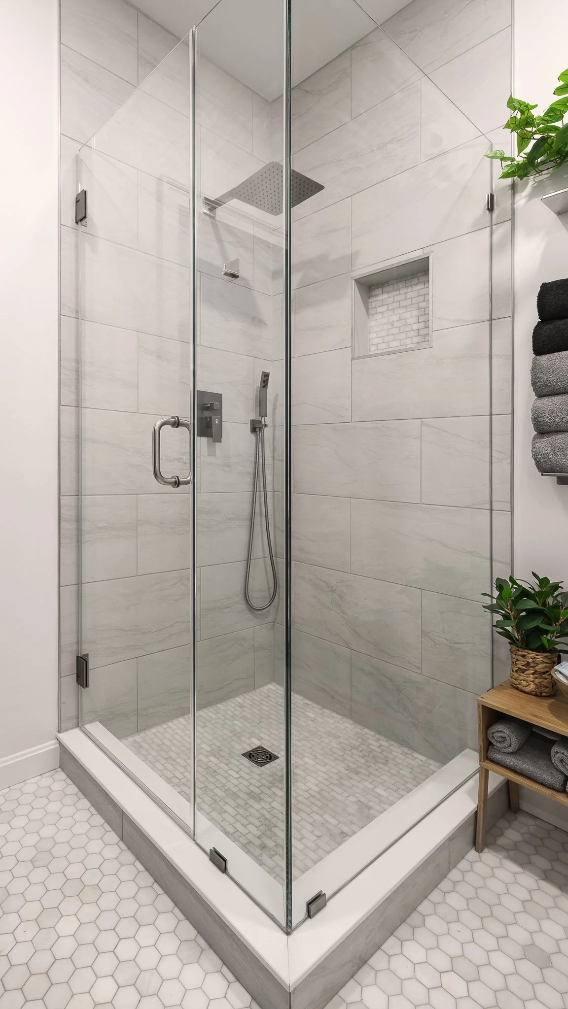 Glass shower stall with gray wall tile and hexagon floor tile.