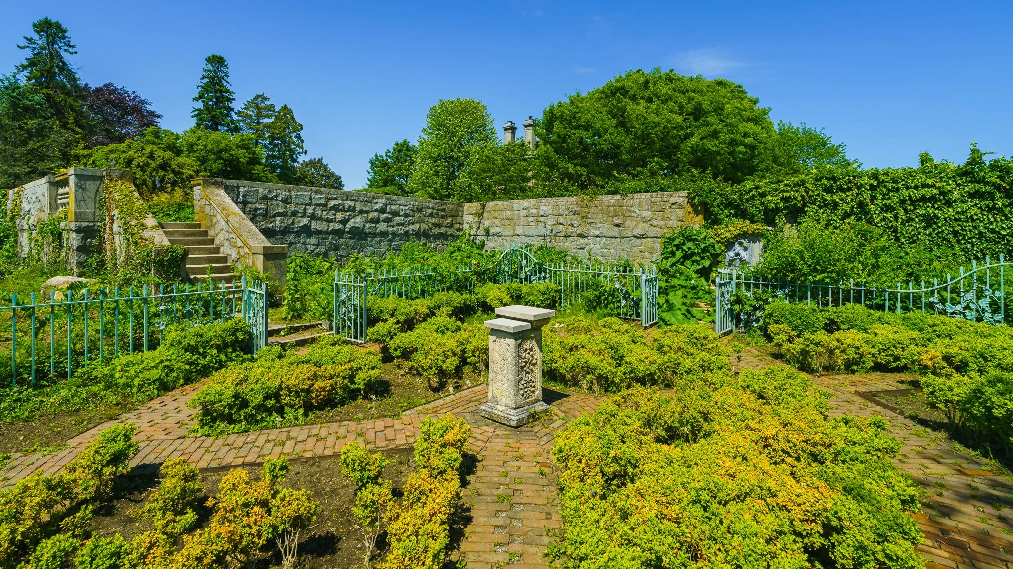 Bird bath at the center of a formal garden with the mansion's garden walls beyond.