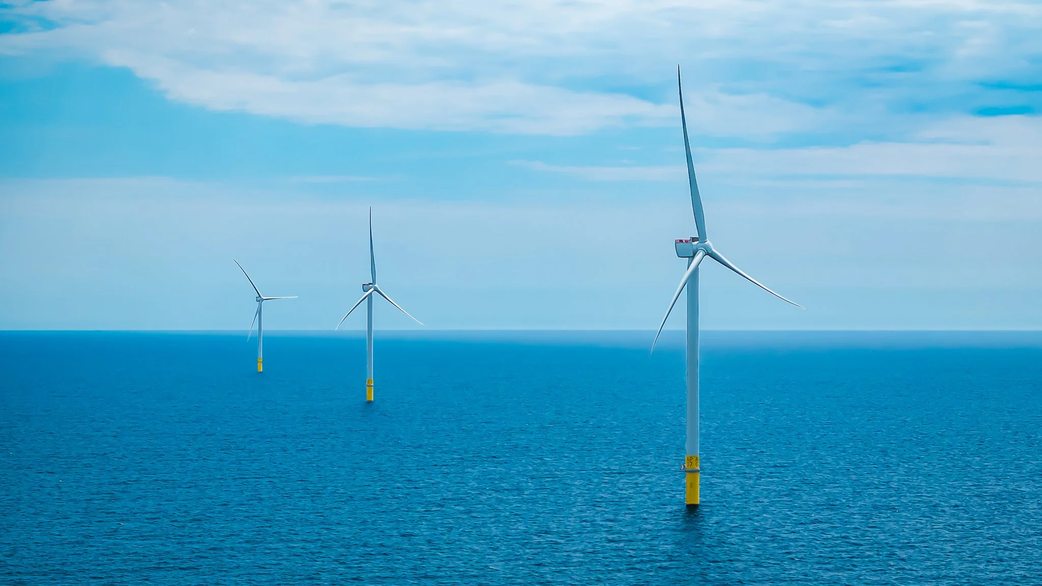 Three wind turbines over teal water, one in front and two farther back.