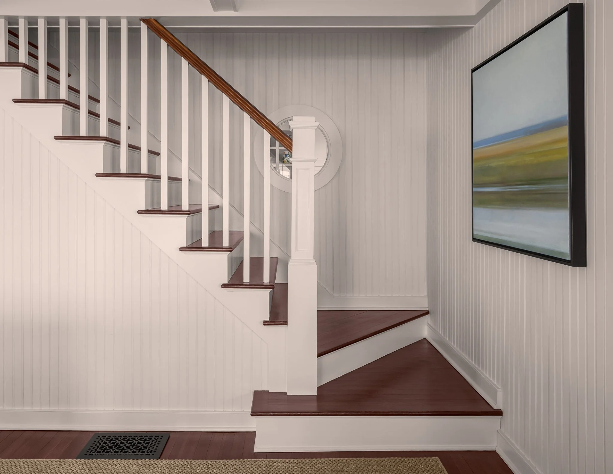 White staircase with dark wood treads beside a large landscape painting.